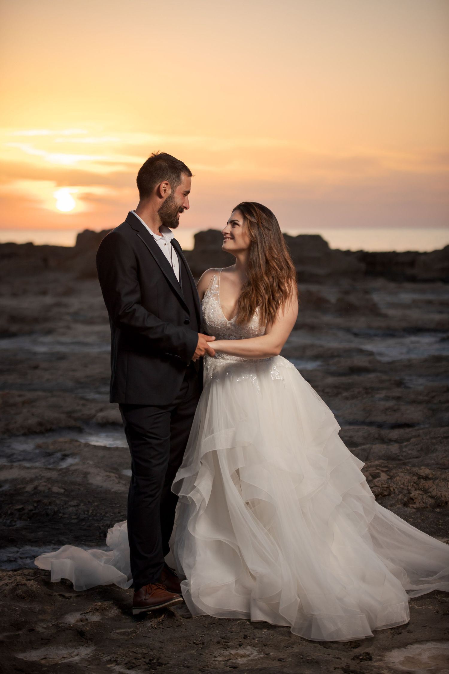 Romantic sunset beach photoshoot with dramatic waves crashing in background.