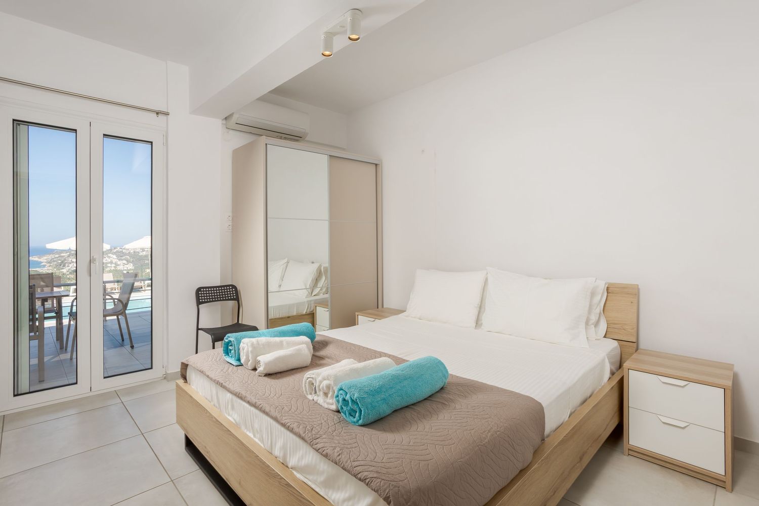 Clean modern bedroom with white linens, turquoise accents, and glass doors leading to a balcony.