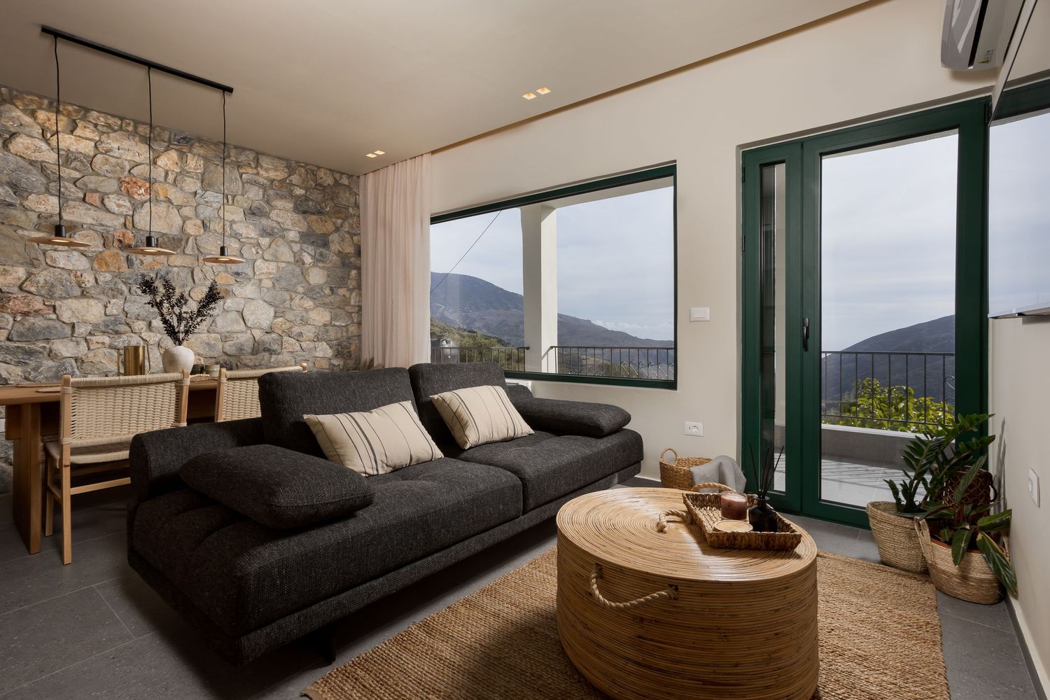 Modern living room interior with stone accent wall, black sofa and panoramic mountain views through large windows.