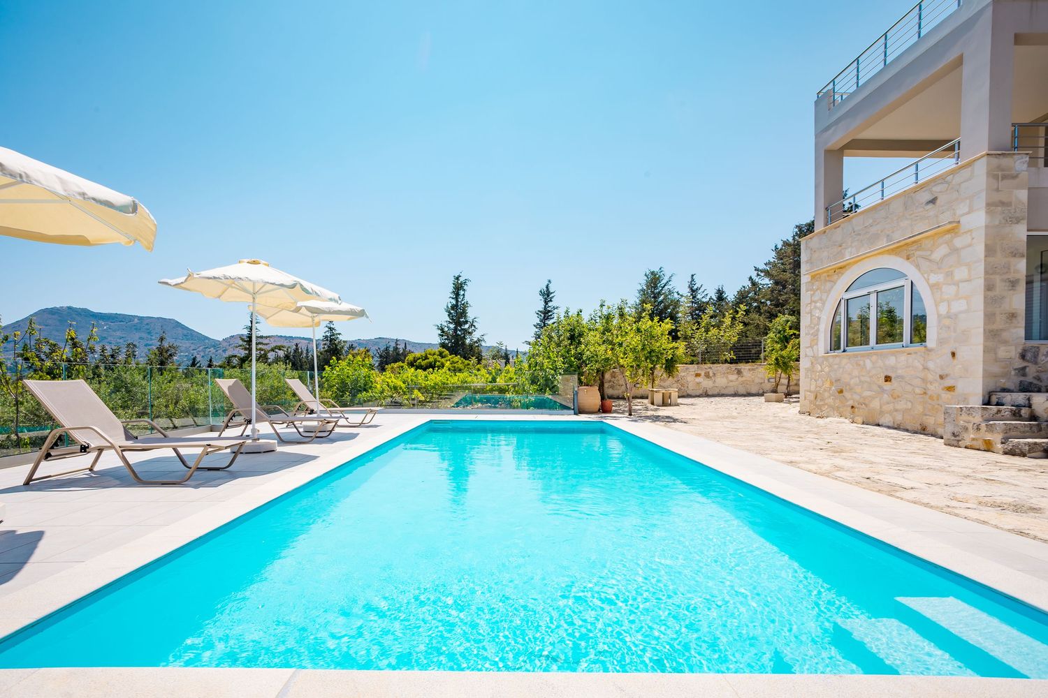 Inviting infinity pool overlooking scenic mountain landscape with lounge chairs and parasols by luxury villa.