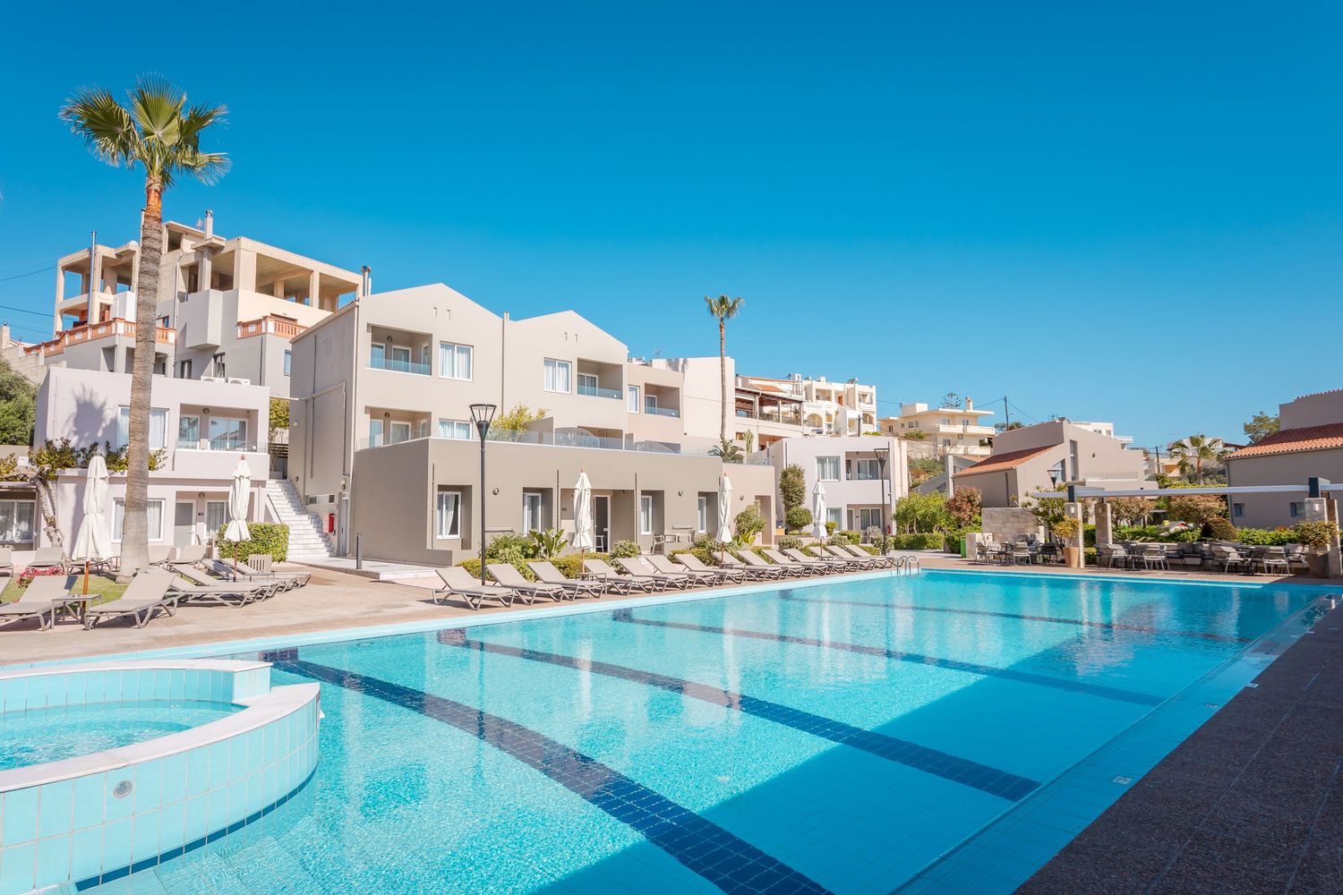 Modern resort hotel with expansive blue swimming pool and white buildings under clear sky.