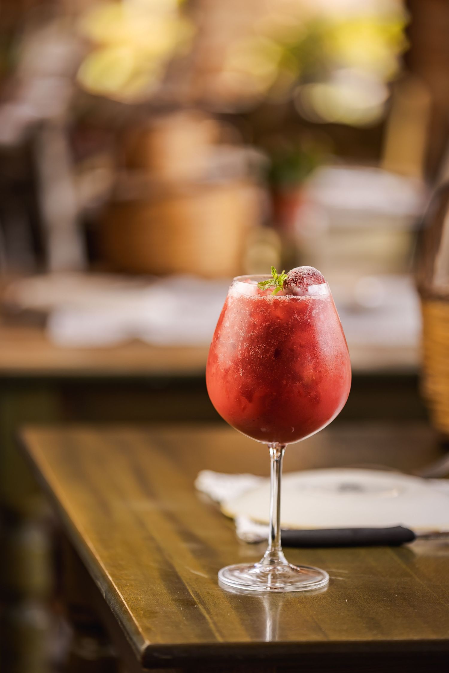 Red frozen cocktail served in a coupe glass on a dark wooden bar counter.