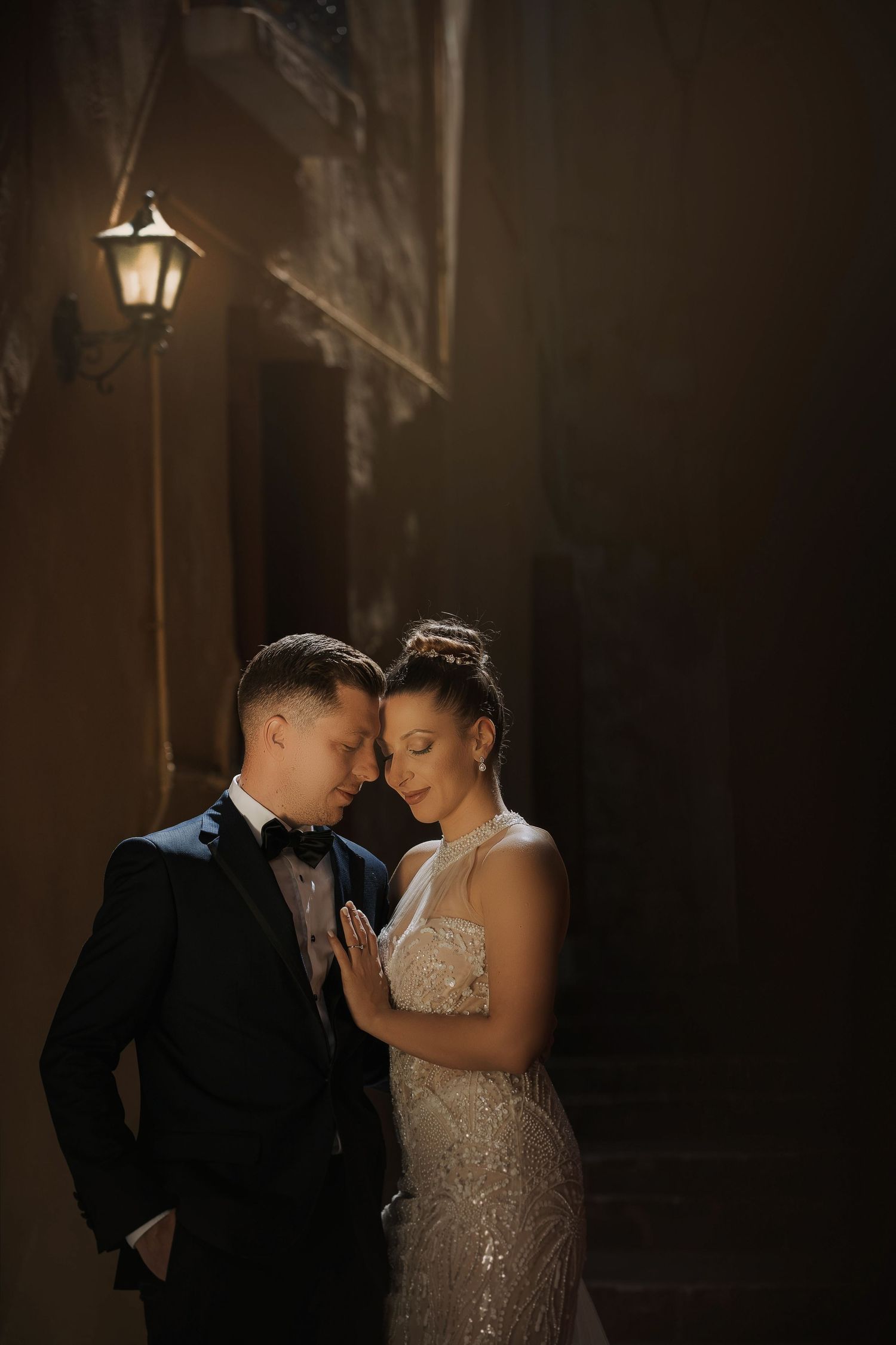 Romantic evening portrait of newlyweds under dim lantern light in atmospheric setting.