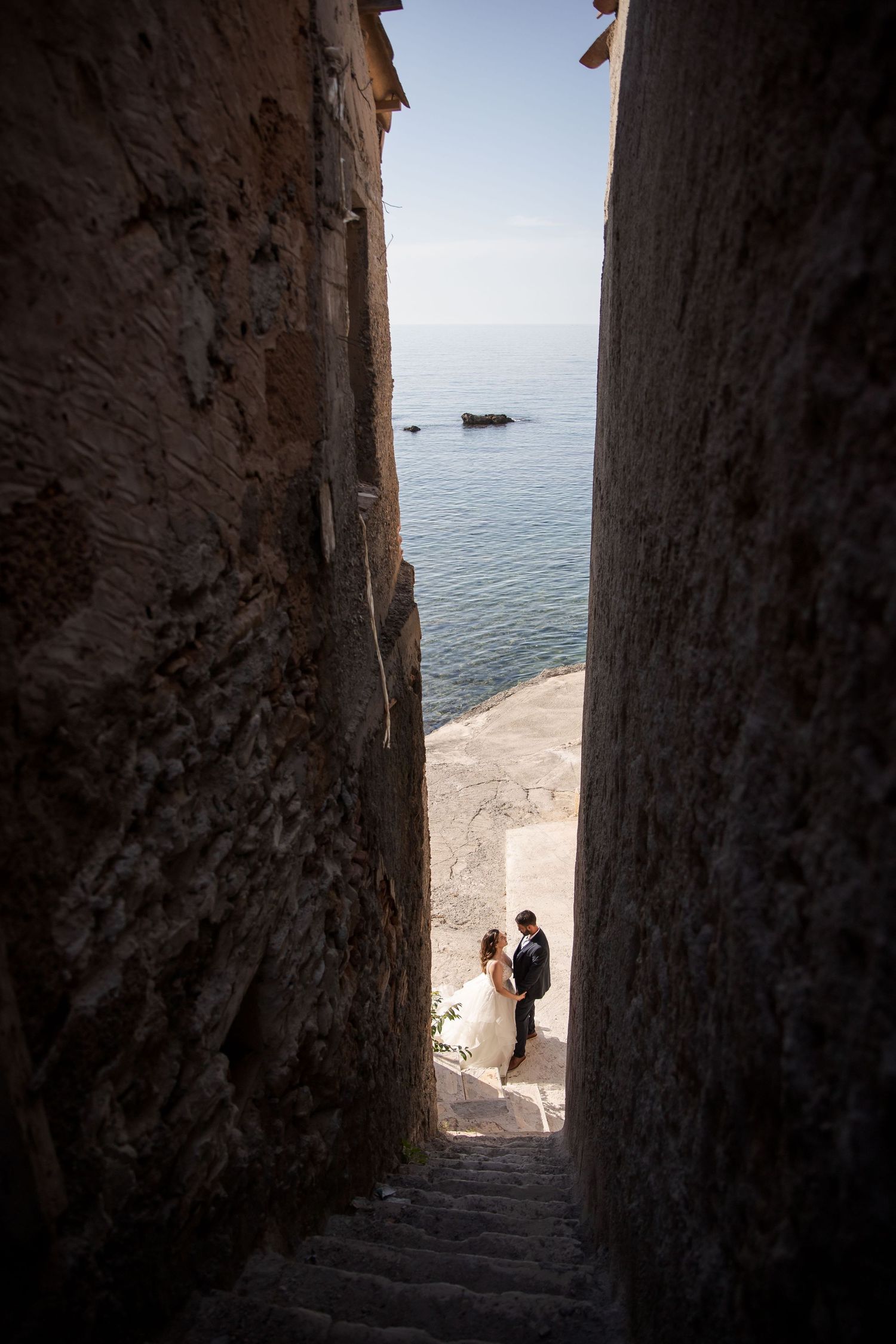 Stone passageway leading to oceanfront terrace creates dramatic wedding portrait composition.