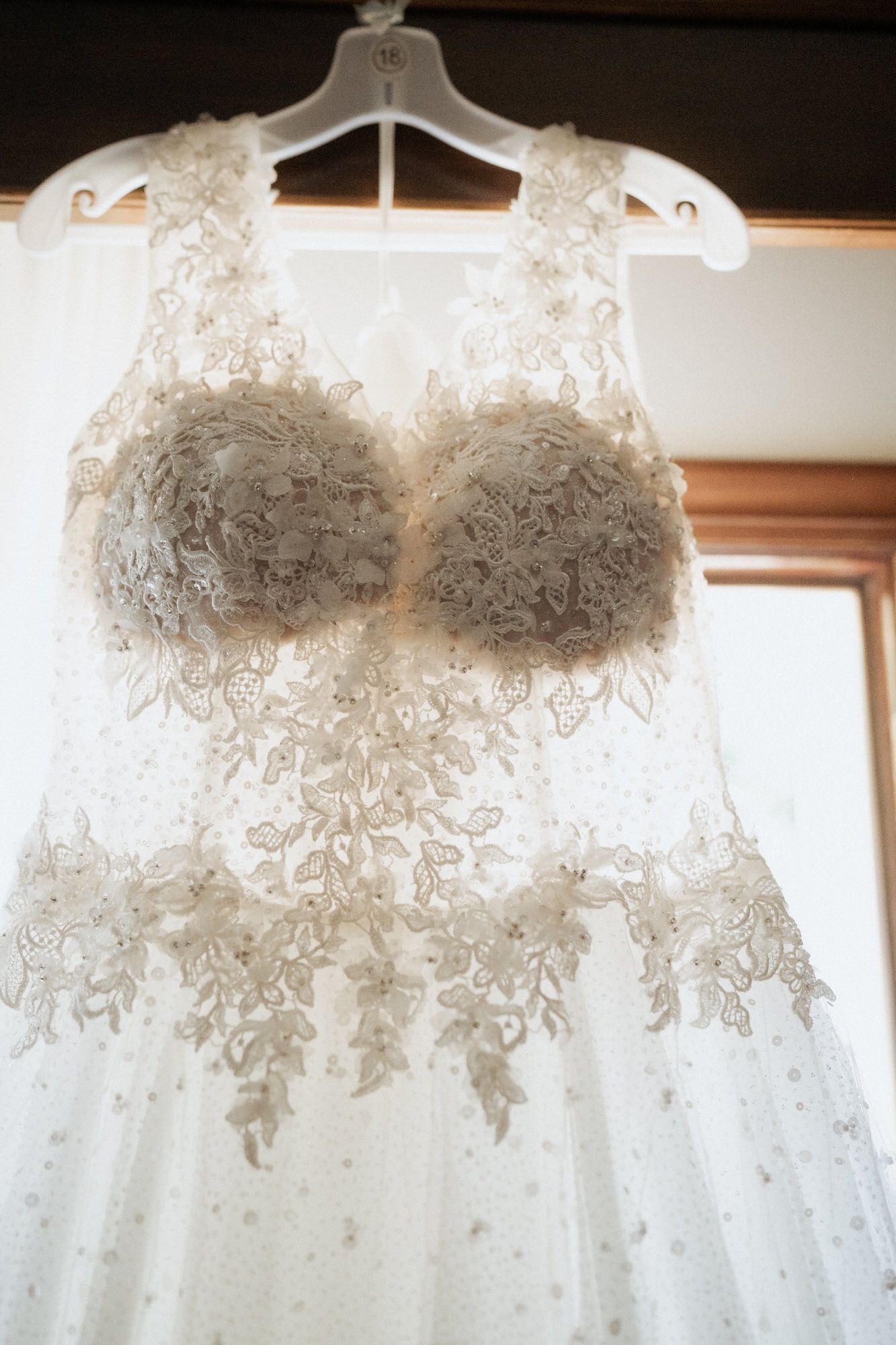 A detailed white wedding dress with intricate lace embellishments hangs on display before the ceremony.