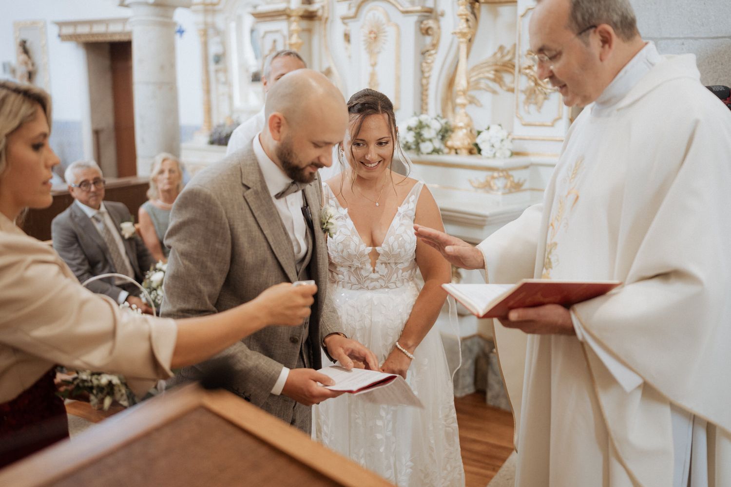 A couple signs paperwork during their wedding ceremony in an ornate church with a priest officiating.