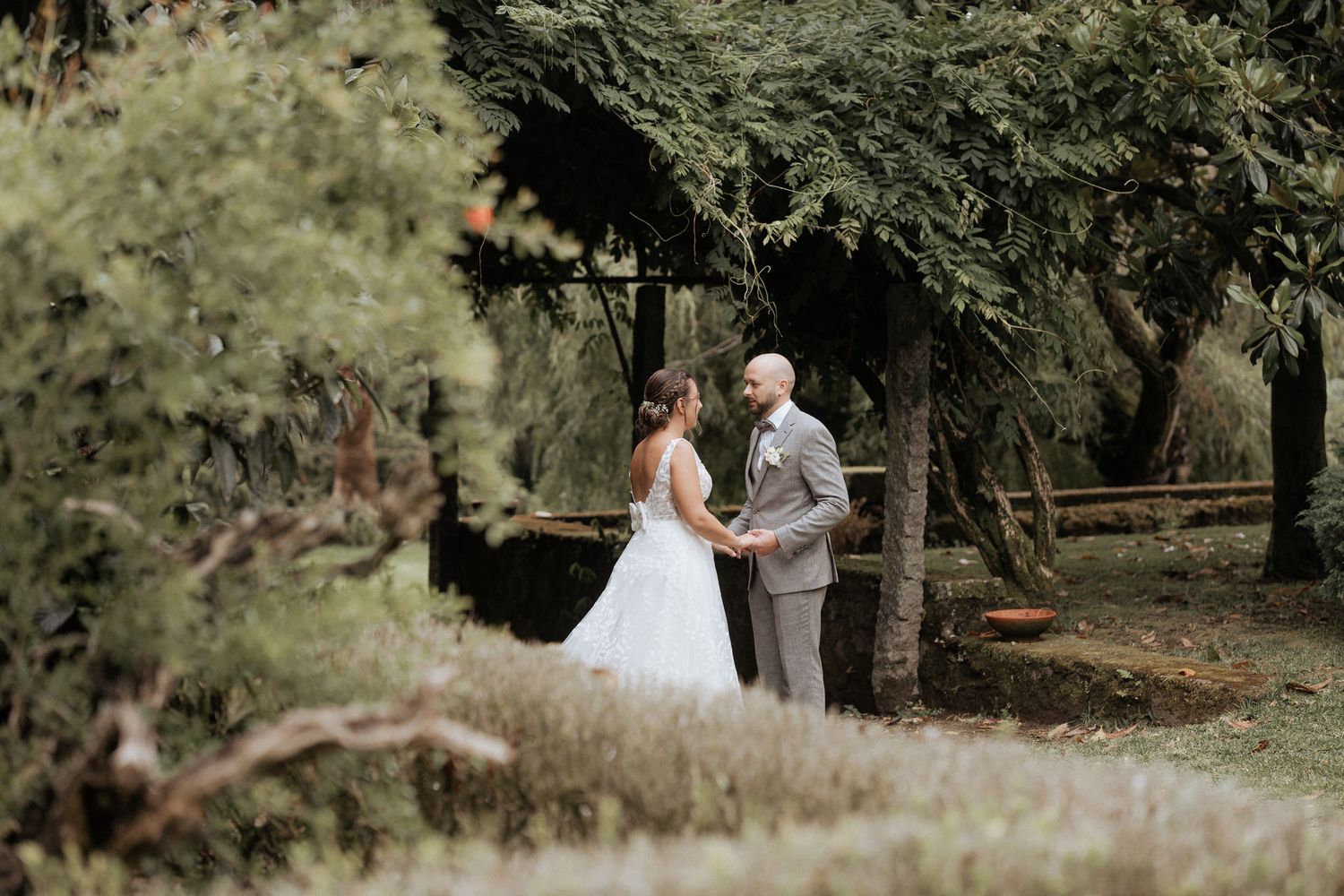 Two people share a tender moment in a wooded outdoor setting surrounded by lush trees and natural light.