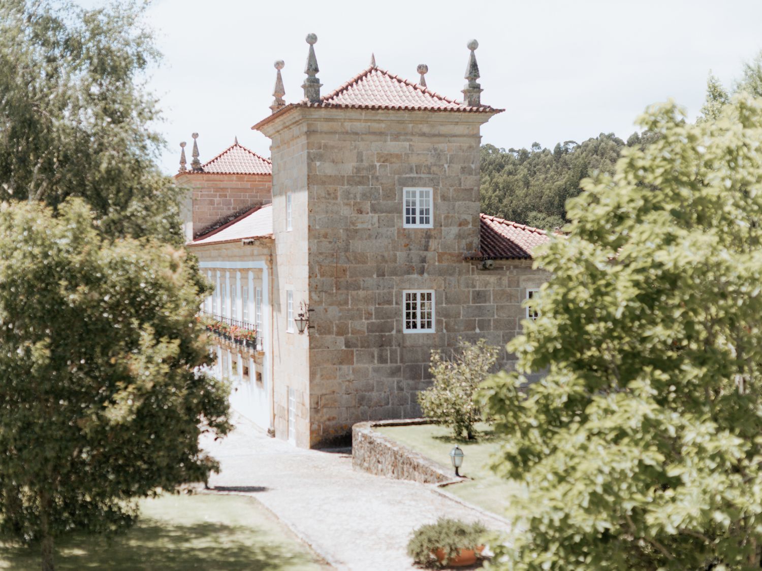 Ancient stone manor house with terracotta roof tiles surrounded by lush greenery in Portugal's countryside estate.