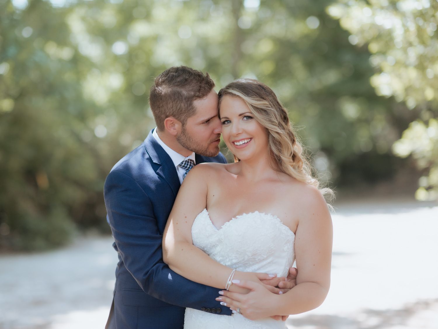 Two people in wedding attire embrace lovingly on a sunlit path in an intimate outdoor moment.