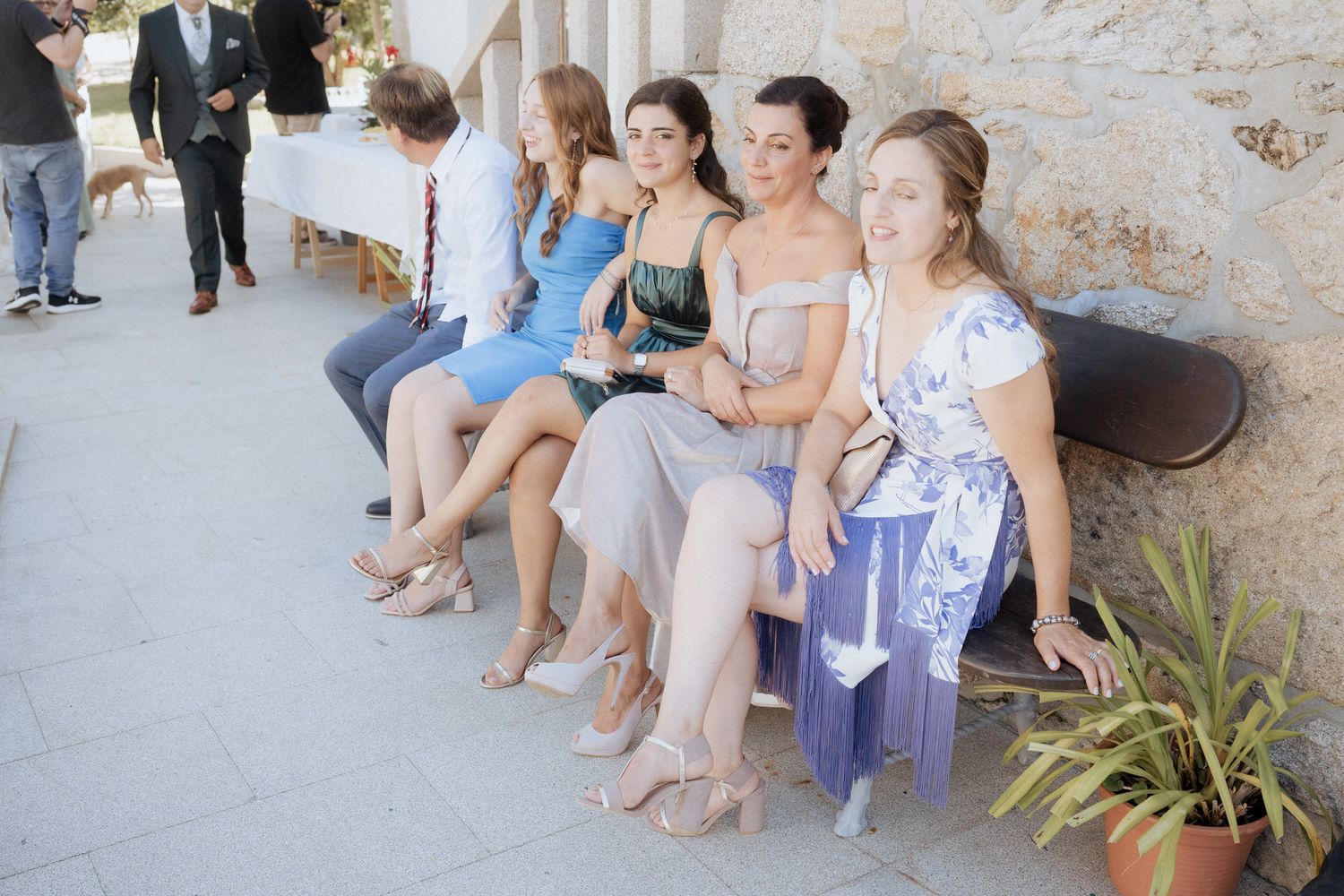 Group of guests sitting together on a stone bench at an outdoor wedding venue.
