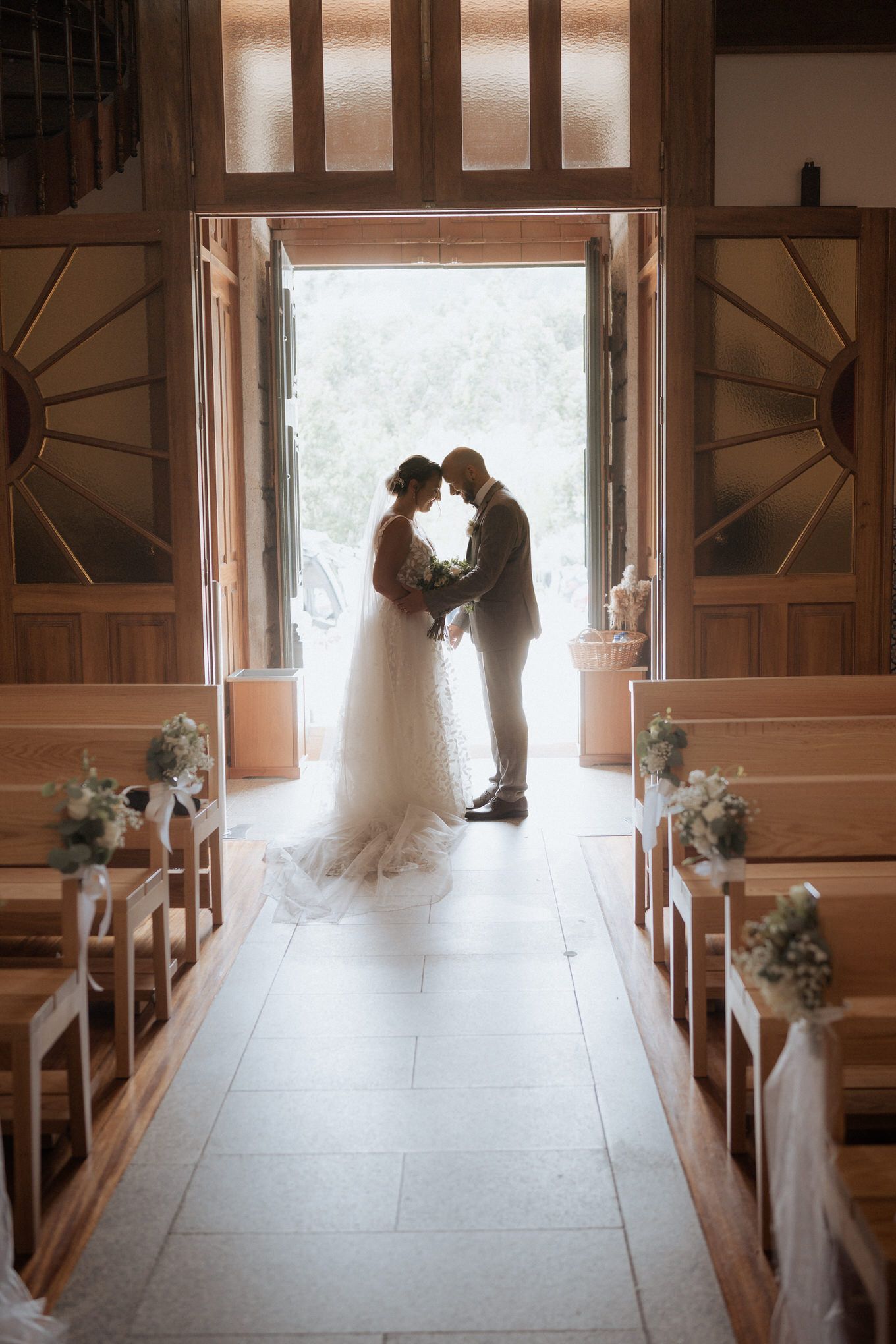 Silhouetted couple shares an intimate moment in the doorway of a church decorated with floral arrangements along the aisle.
