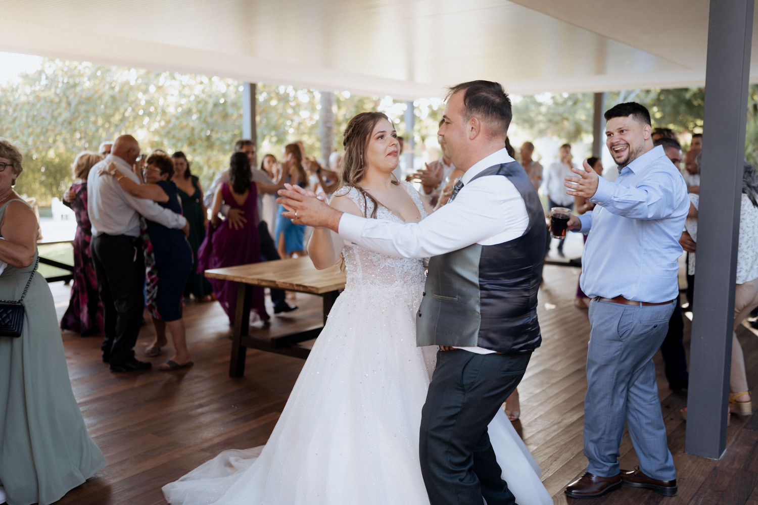 Wedding guests dance together on a covered outdoor patio during a reception celebration.