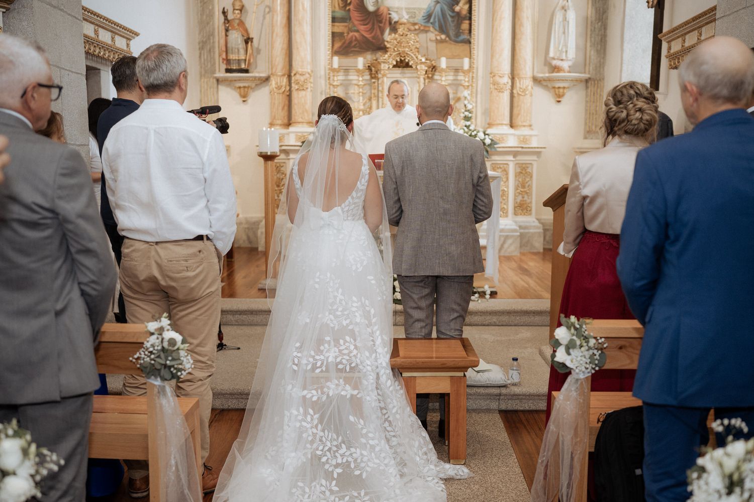 A couple stands at the altar in a Catholic church during a wedding ceremony while guests observe from the pews.
