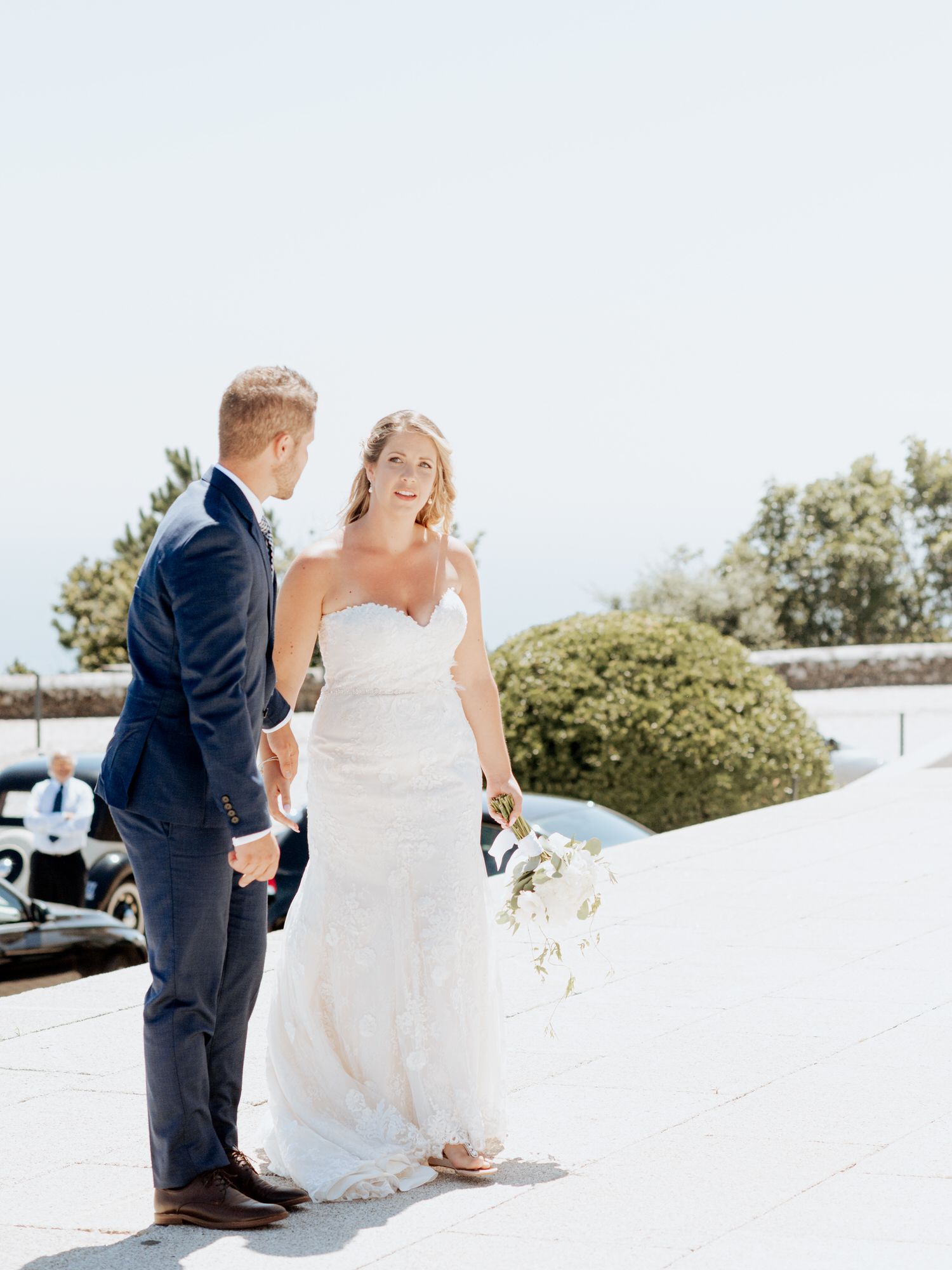 A couple shares a joyful moment together on their wedding day, with the bride wearing a strapless white gown outdoors.