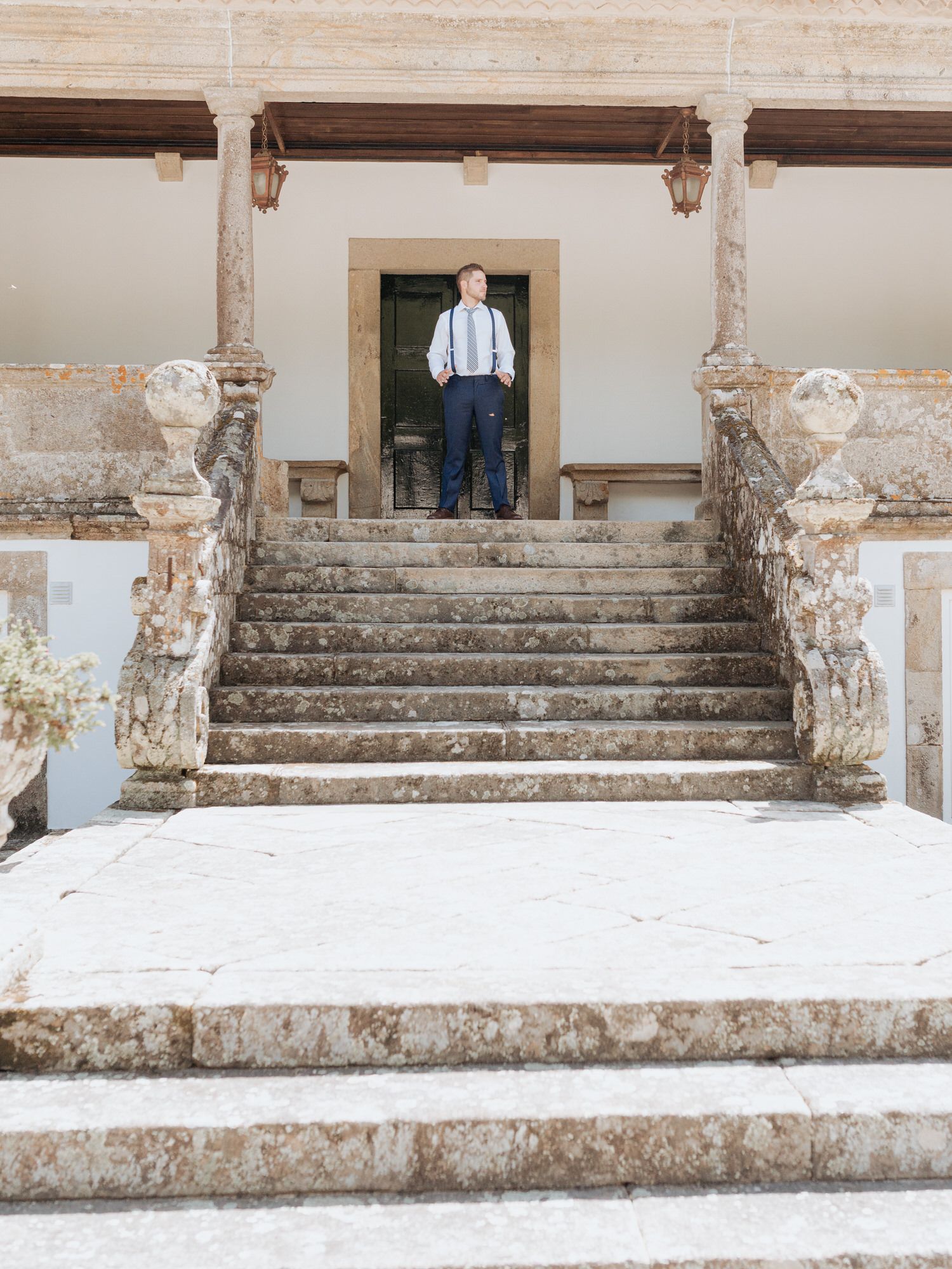 Vintage stone staircase with decorative balusters leads to a doorway where a person in suspenders stands at entrance.