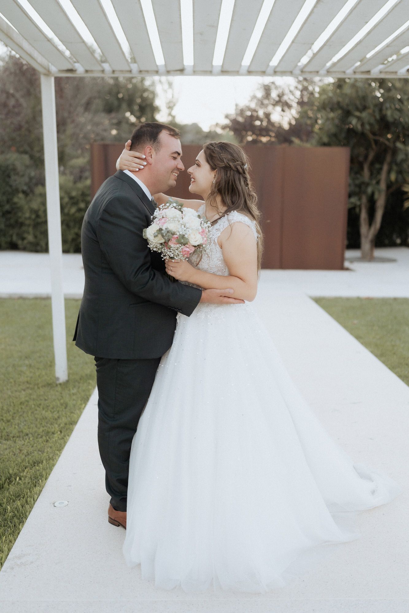 Happy couple sharing a romantic moment under a white pergola at their outdoor wedding celebration.