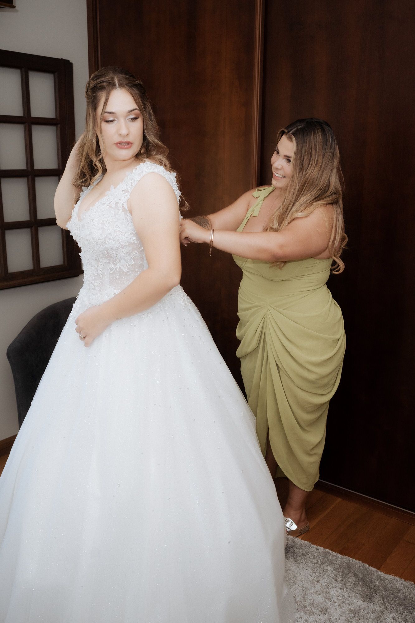 A bride in a flowing white ballgown gets help with final adjustments before the ceremony.