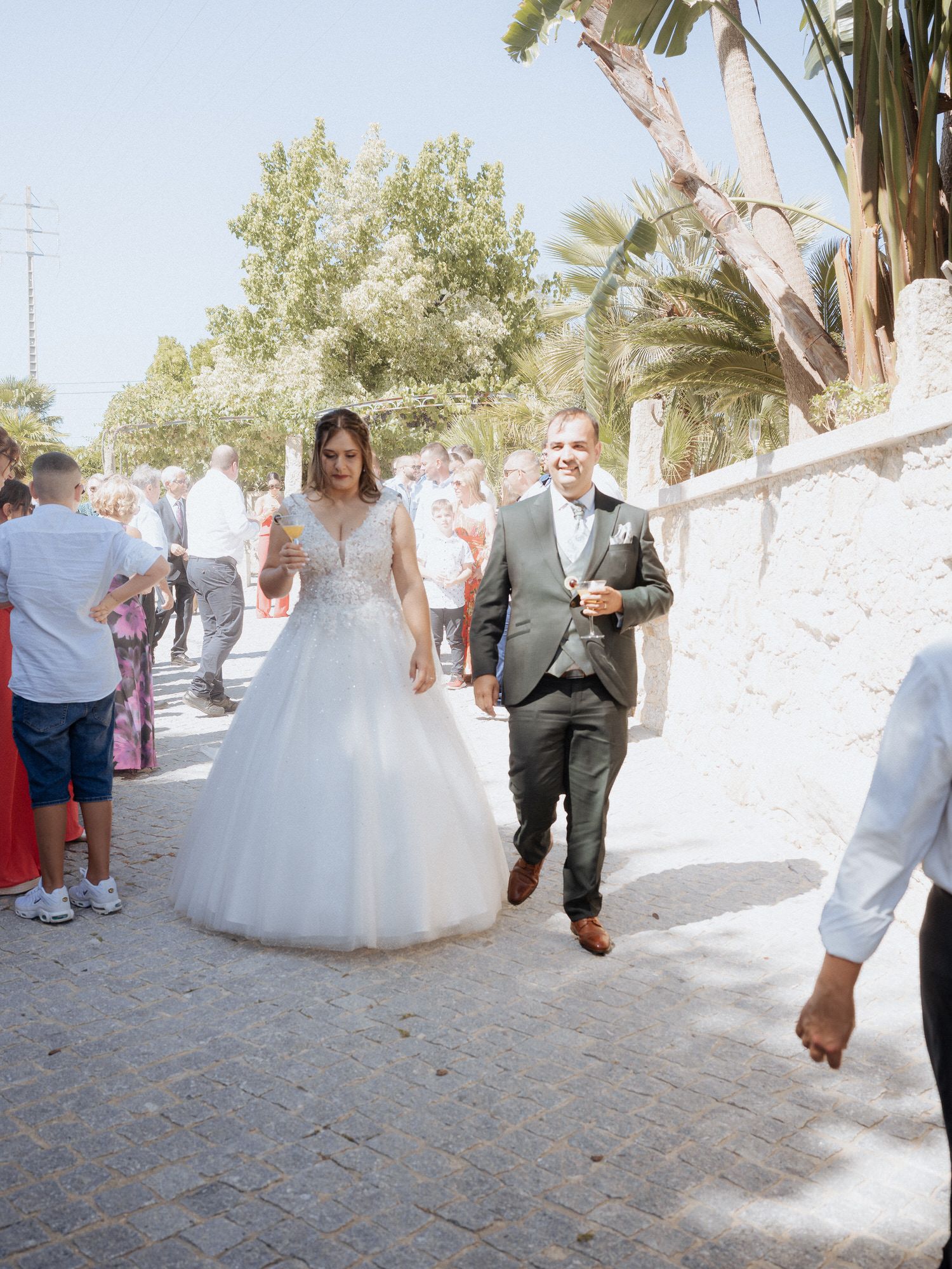 Newlyweds walking together on a sunny path lined with palm trees during their wedding celebration.