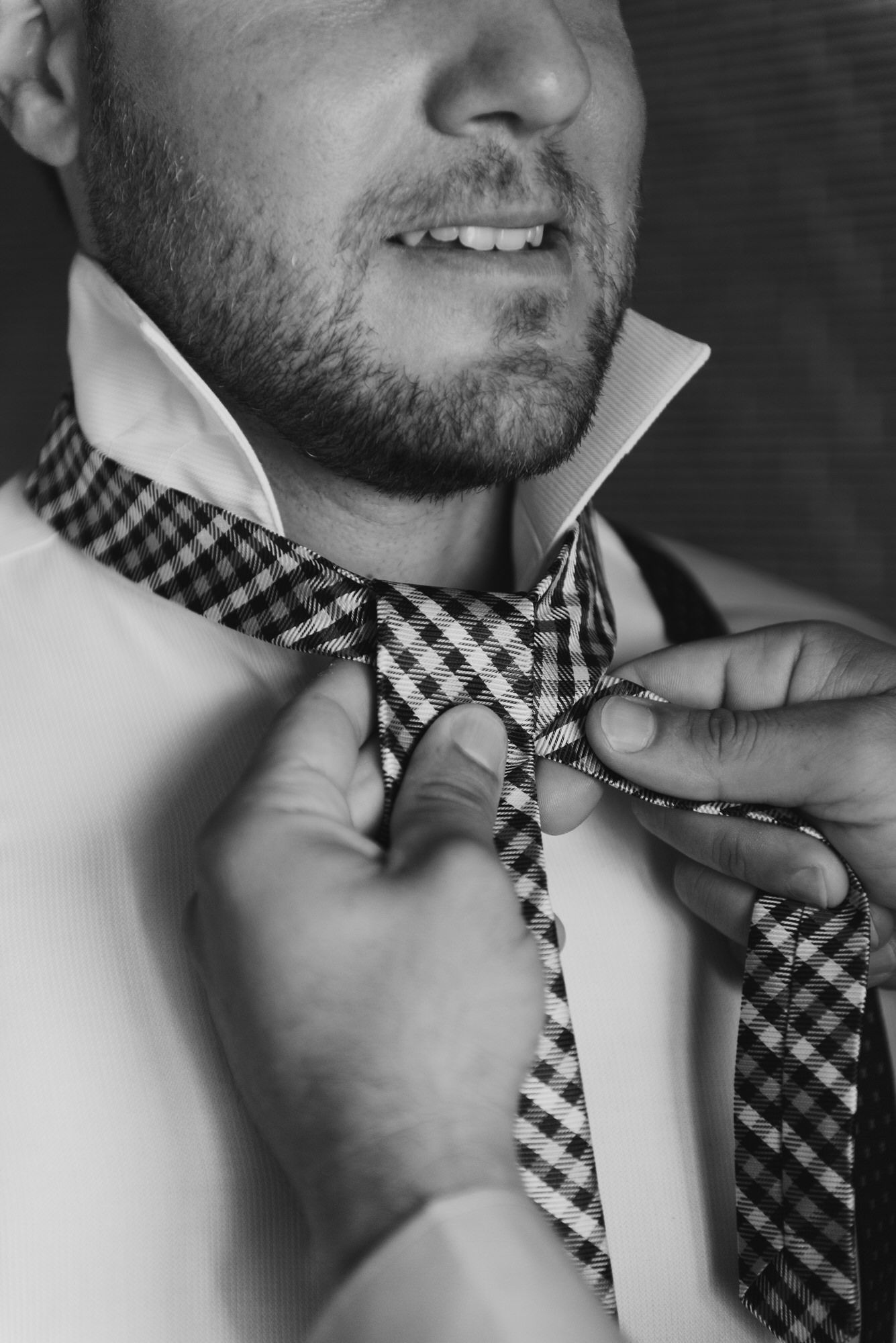 Close-up black and white shot of hands adjusting a checkered bow tie.