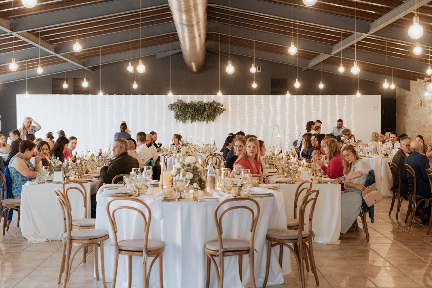 Modern industrial wedding reception venue with white tables, bentwood chairs and hanging pendant lights in historic warehouse.