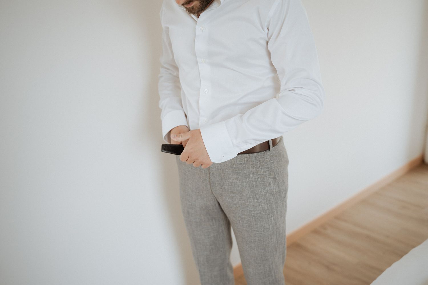 A person wearing a crisp white dress shirt and gray checkered pants stands against a white wall with hardwood flooring.