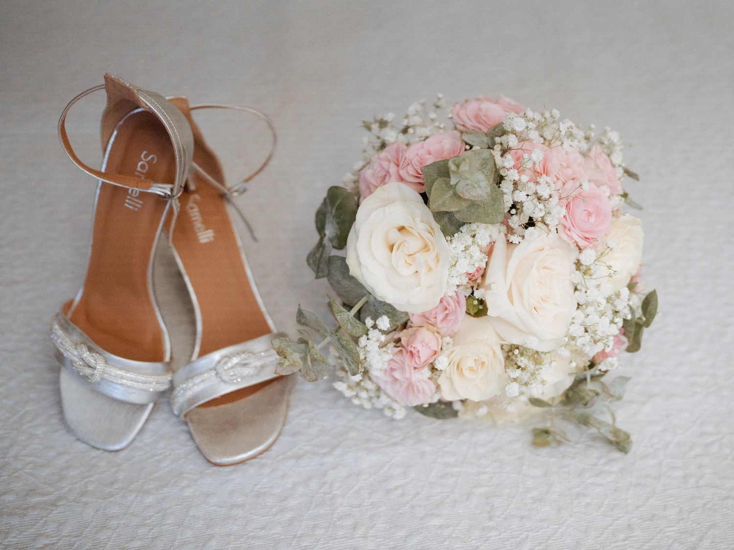Bridal shoes paired with a romantic bouquet of pink and white roses with delicate baby's breath.