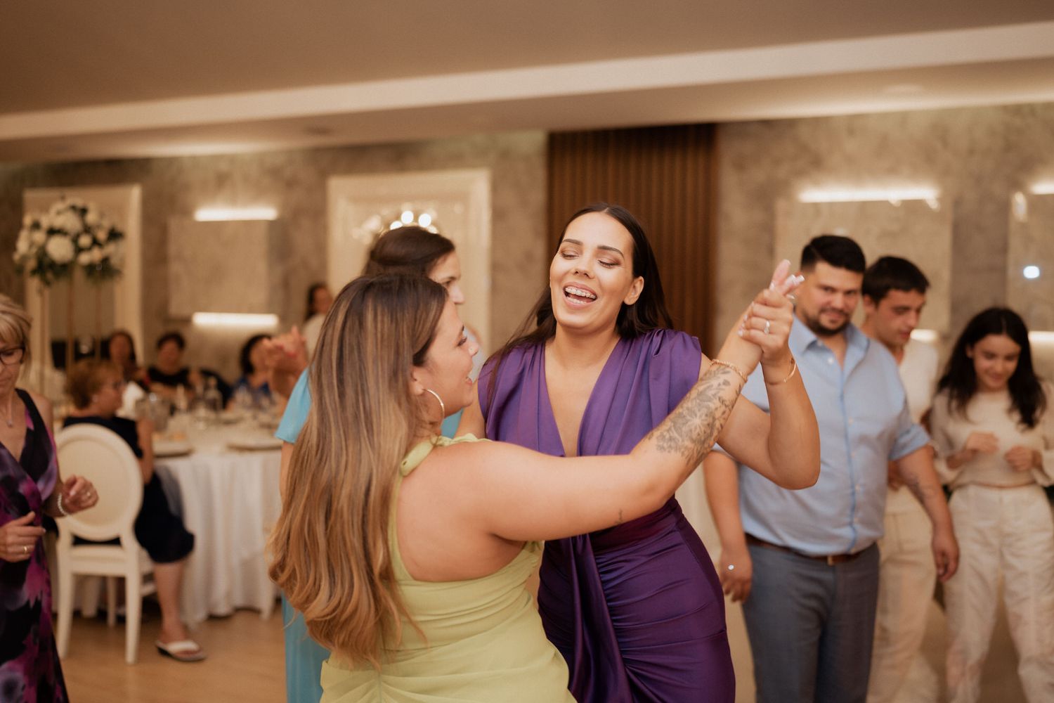 Wedding guests dance and celebrate together at a joyful reception in a bright ballroom.