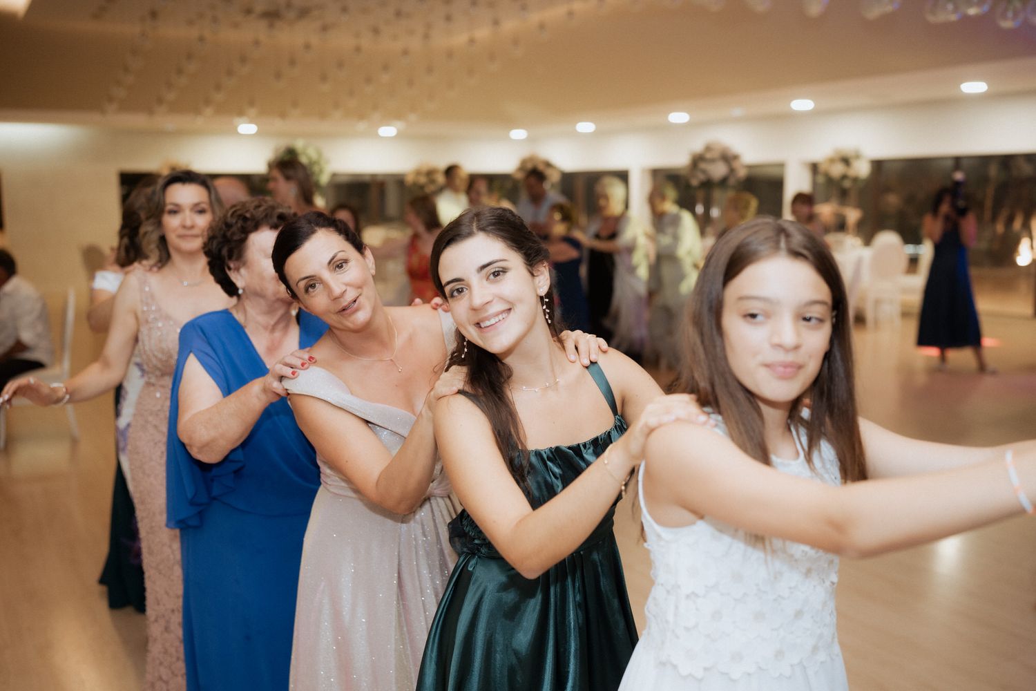 Party guests line up in colorful formal attire for a fun dance move at an elegant indoor reception venue.