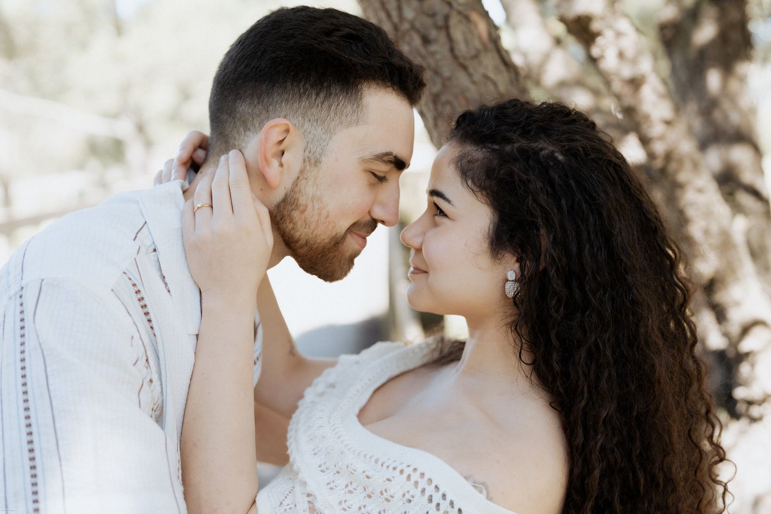 Um casal romântico em trajes brancos partilha um momento íntimo ao ar livre sob uma suave iluminação natural.