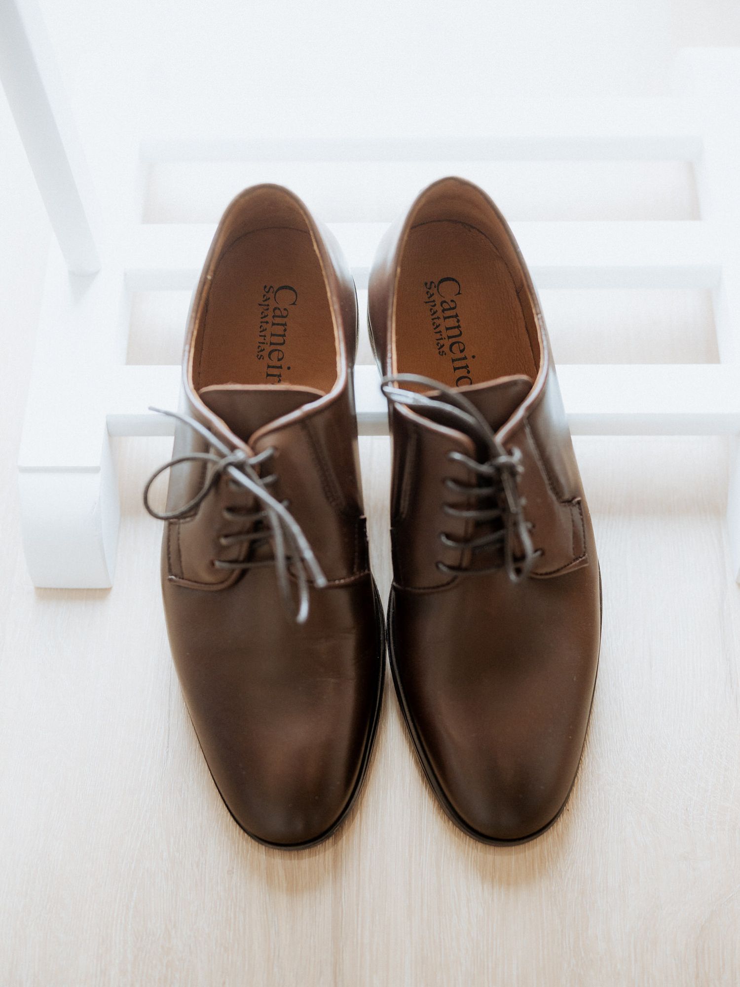 A pair of classic brown leather dress shoes with gray laces sits on a white surface.