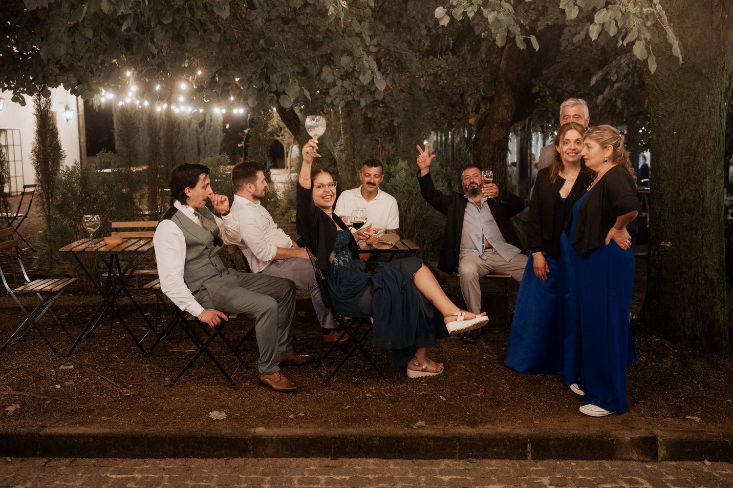 Wedding party relaxing outdoors under string lights during an evening celebration.