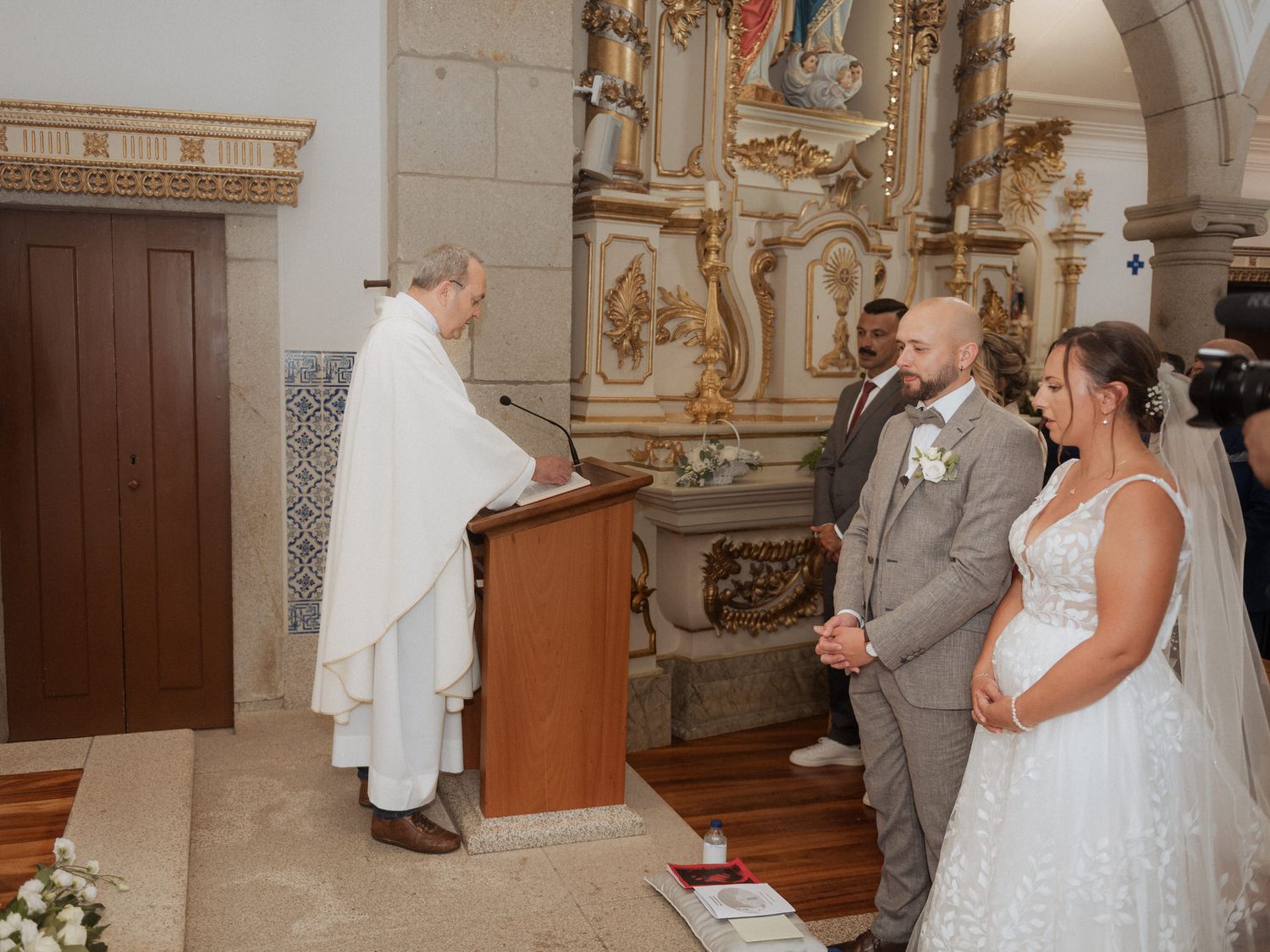 Religious ceremony taking place in an ornate church with a couple standing before a robed clergy member at the altar.