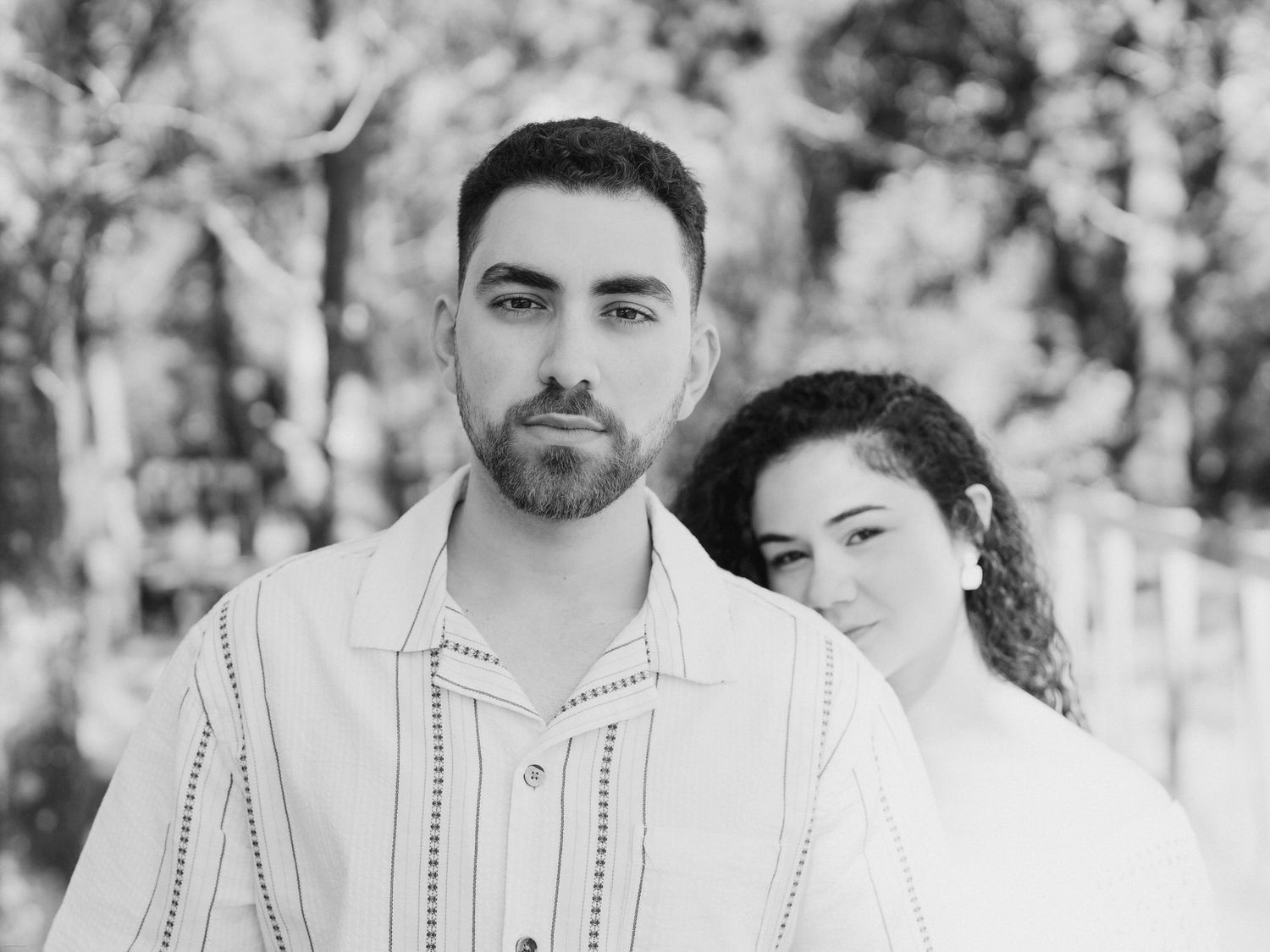 Retrato a preto e branco de um casal num cenário de floresta com fundo bokeh suave.