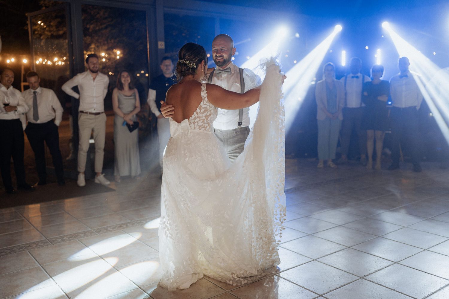 A couple shares their first dance as newlyweds under dramatic lighting on a white dance floor at their wedding reception.