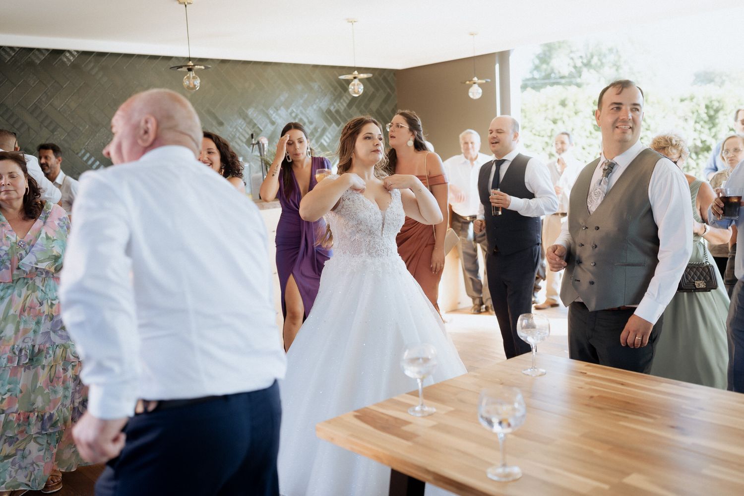 Wedding guests dance together at a reception venue with wooden tables and festive decor while celebrating special occasion.