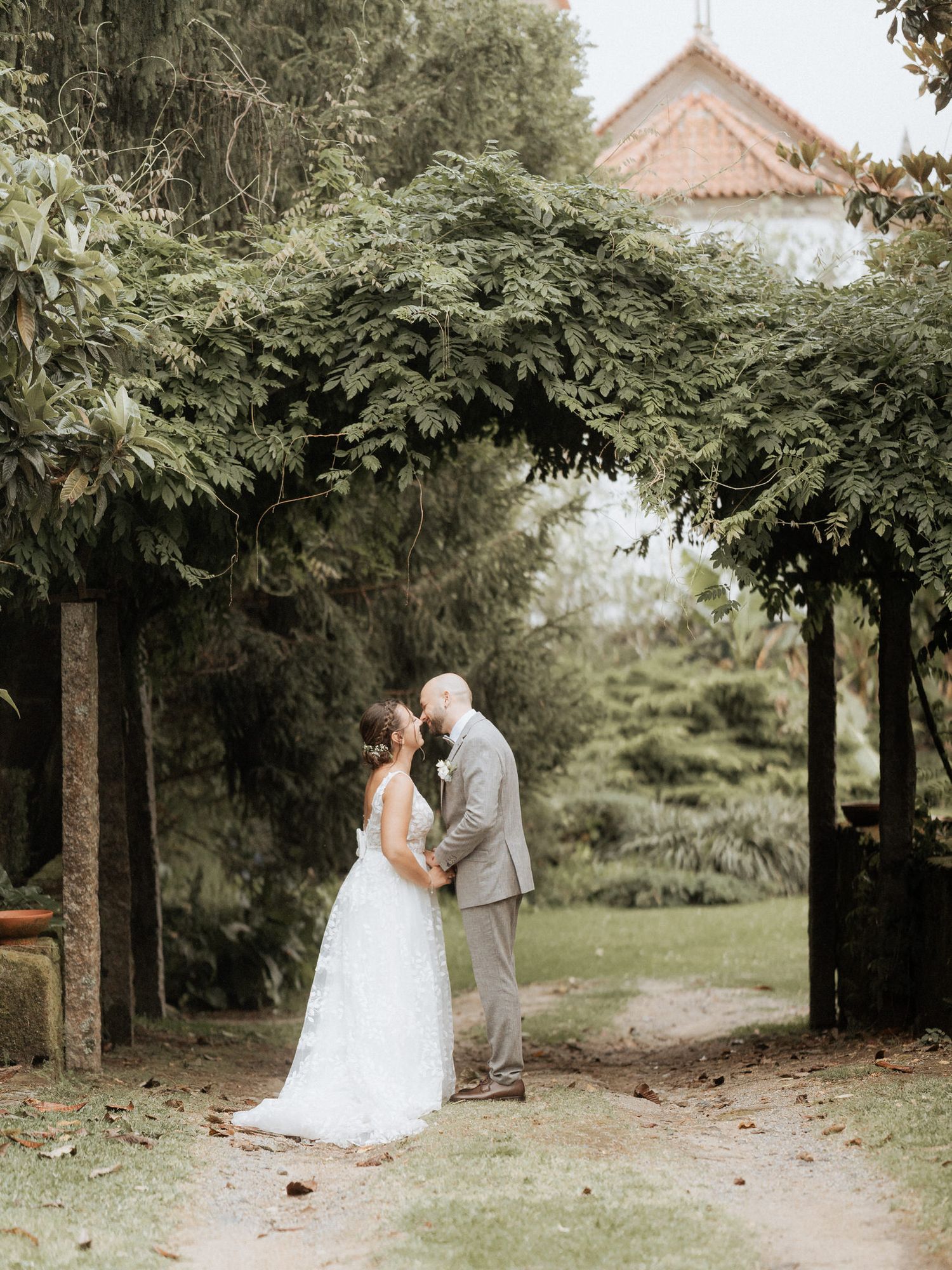 A couple in wedding attire shares a romantic moment under a beautiful garden archway with lush greenery.