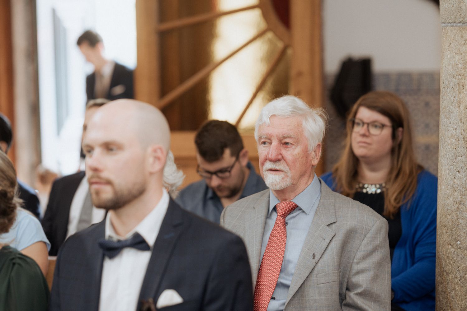 Attendees gather in a bright interior space for a formal event with someone in a bow tie in the foreground.