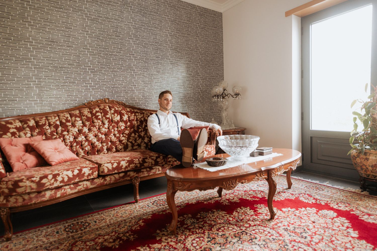 A person relaxes on a vintage brown tufted sofa in a living room with gray brick wall and red oriental rug.