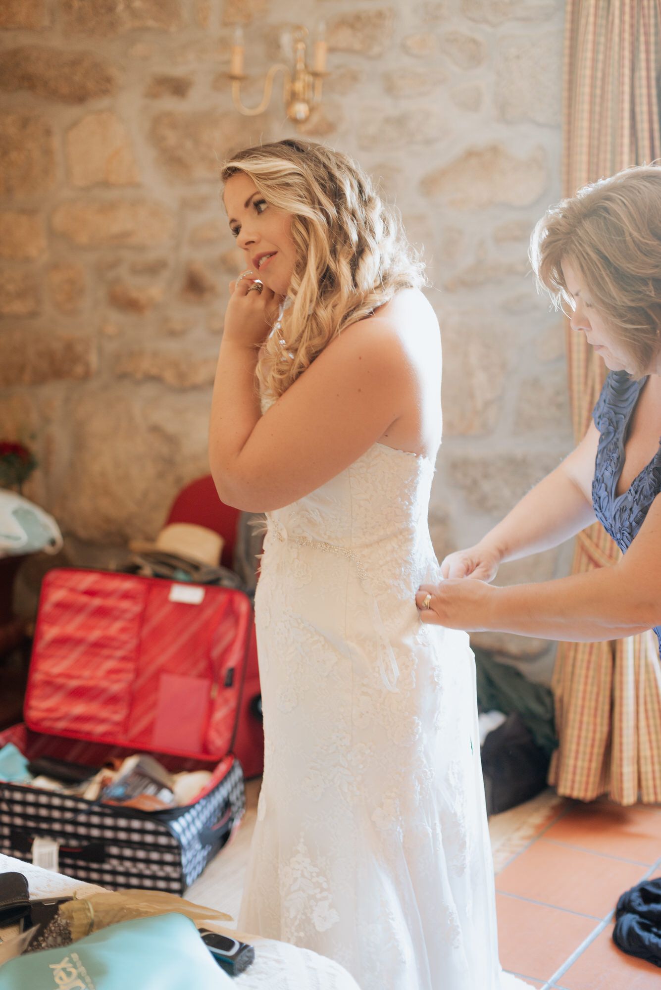 A sequence showing someone being helped into a white lace wedding dress in a rustic stone room.