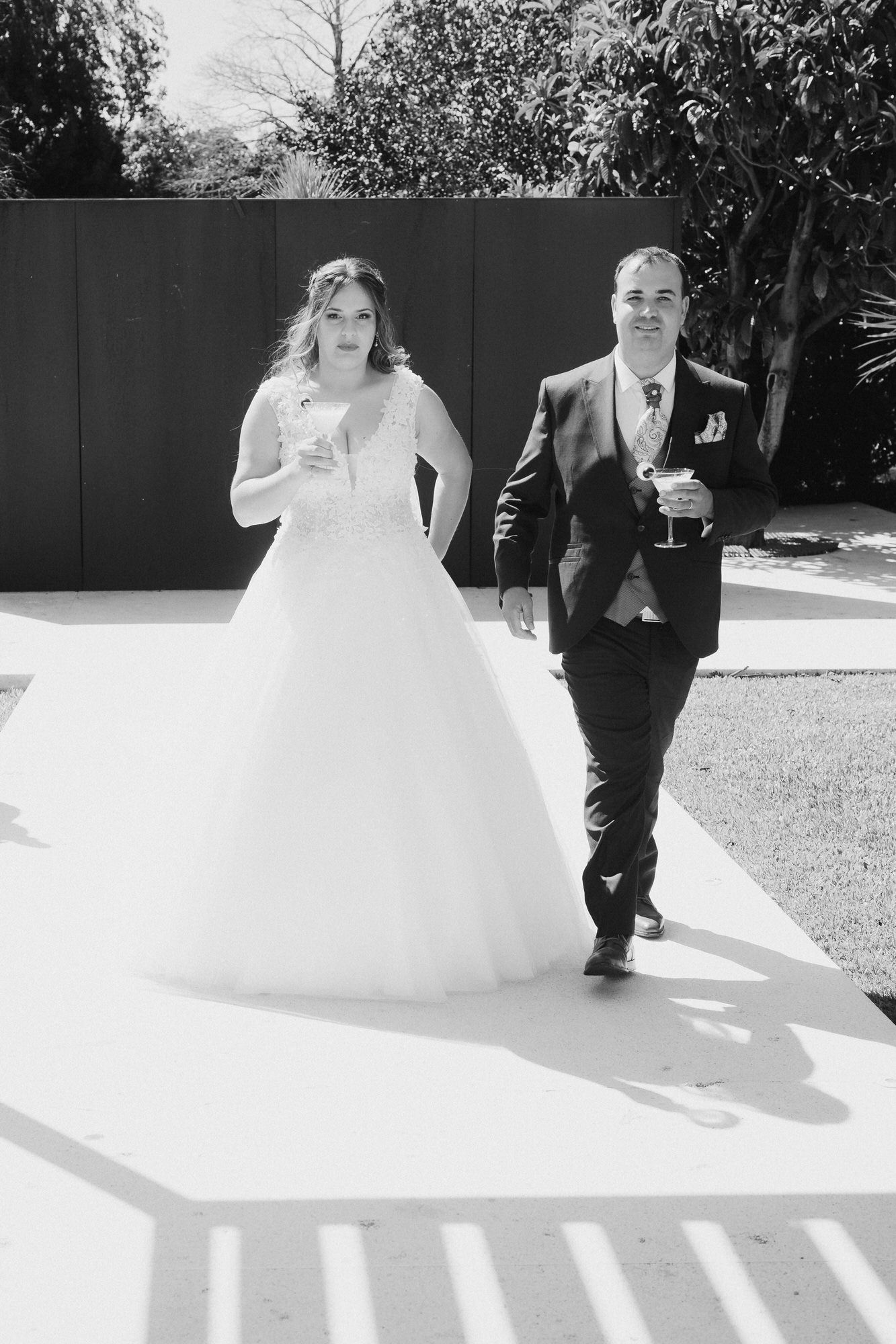 A couple walk together on a sunlit path, with the bride wearing a flowing white ball gown.