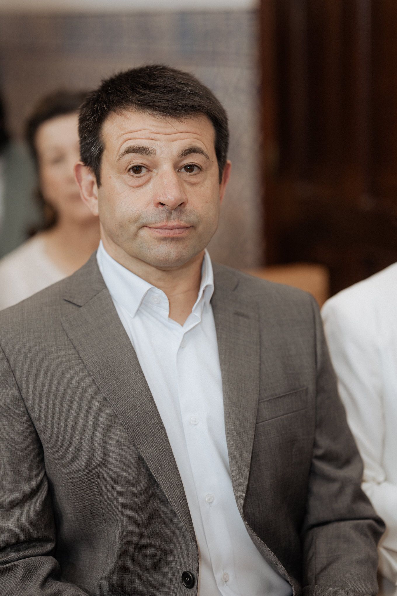 Professional wearing a brown suit jacket and white dress shirt poses for a business portrait.