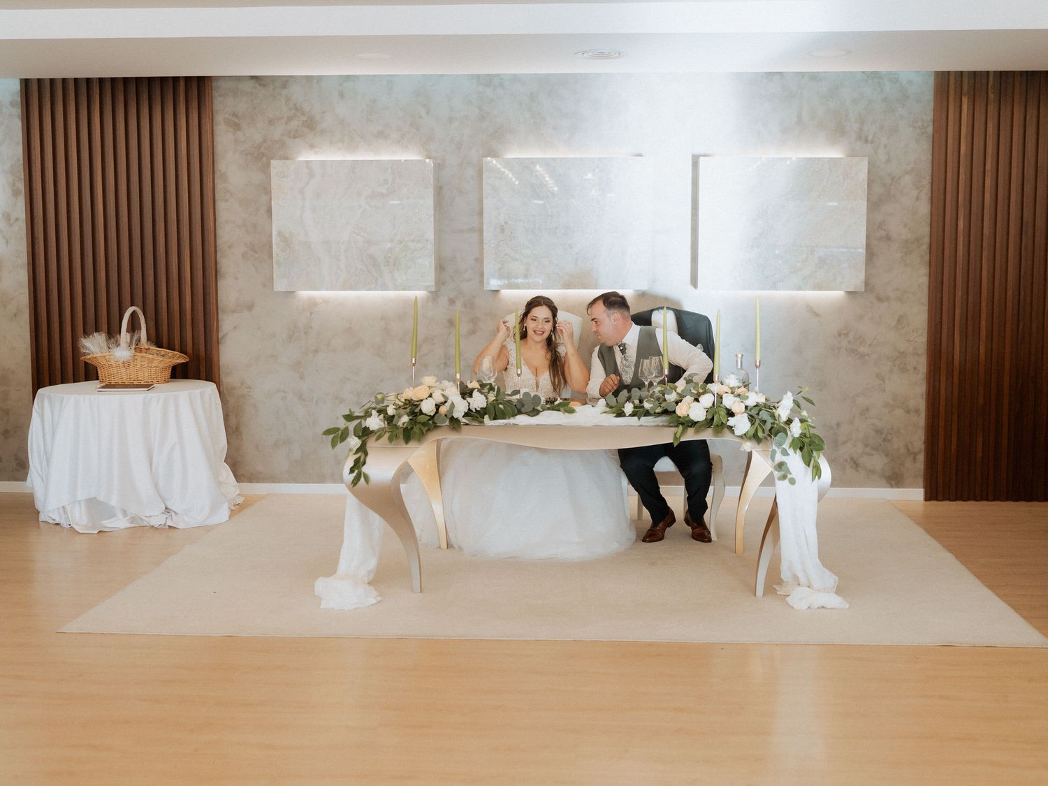 Elegant wedding reception setup featuring a head table adorned with white floral arrangements in a modern banquet room.