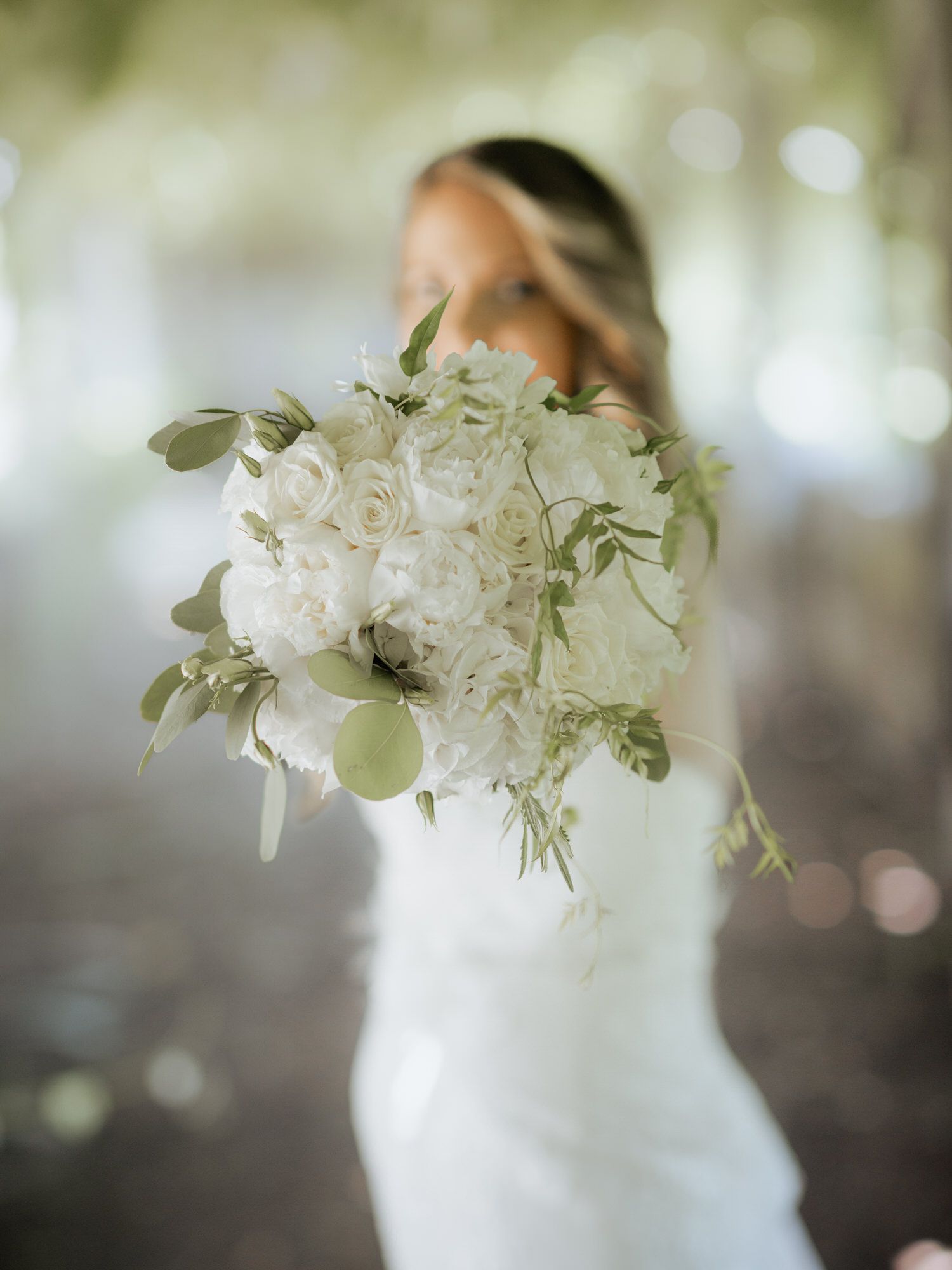 A dreamy bridal photo showing an elegant white bouquet of roses and greenery against a soft bokeh background.