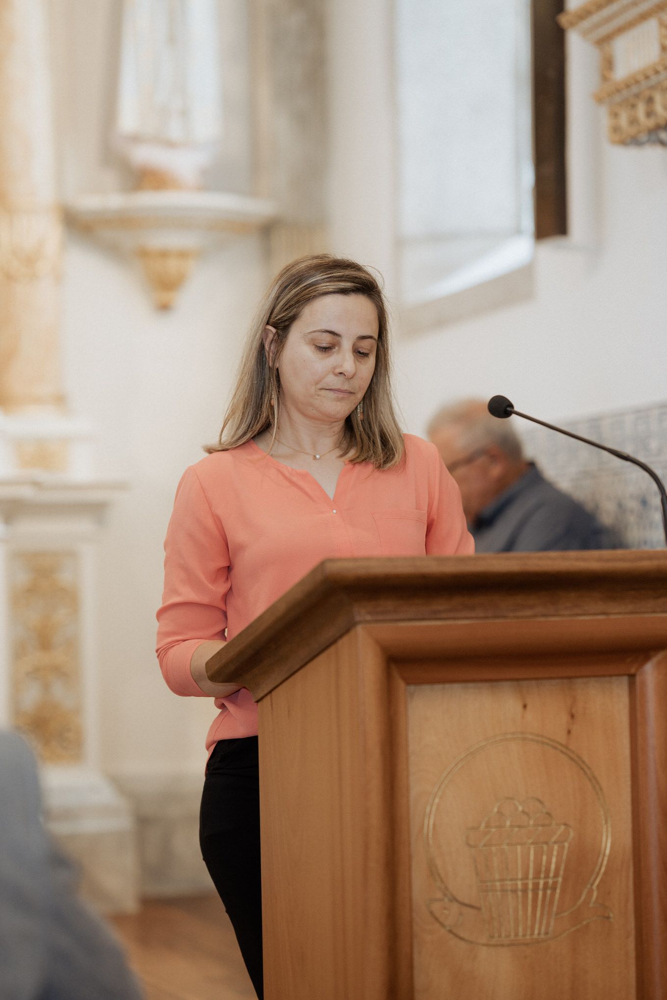 A person in a coral-colored top stands at a wooden podium during a church service.