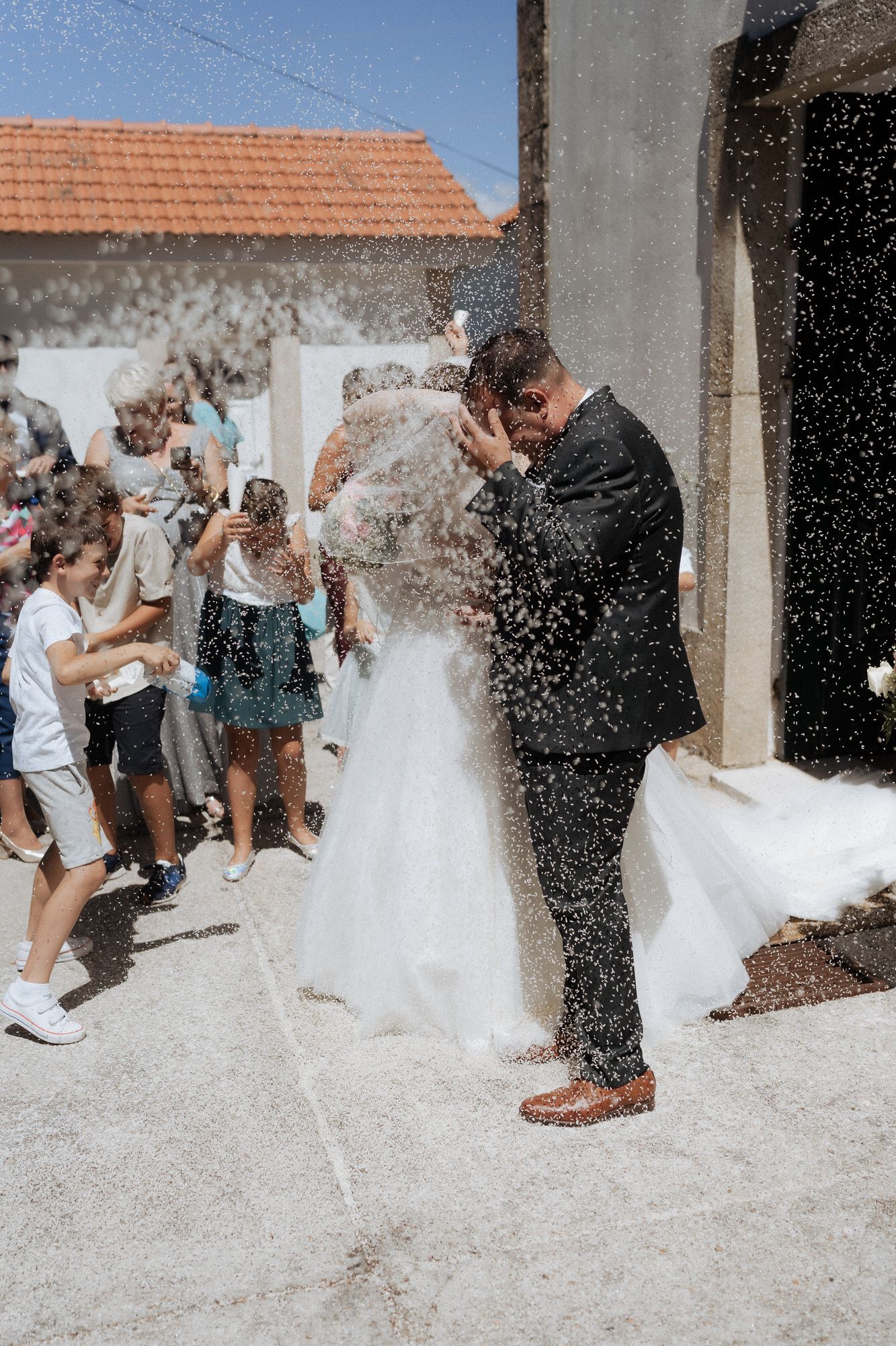 A wedding couple and guests enjoy playful moments as white powder is thrown in a joyful celebration outside a venue.