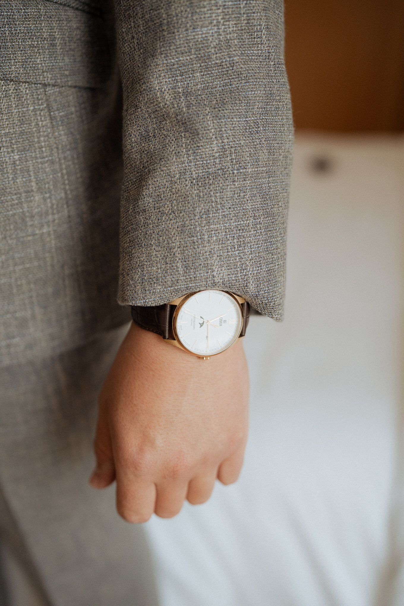 A minimalist white watch face with brown leather strap worn with a grey suit sleeve.