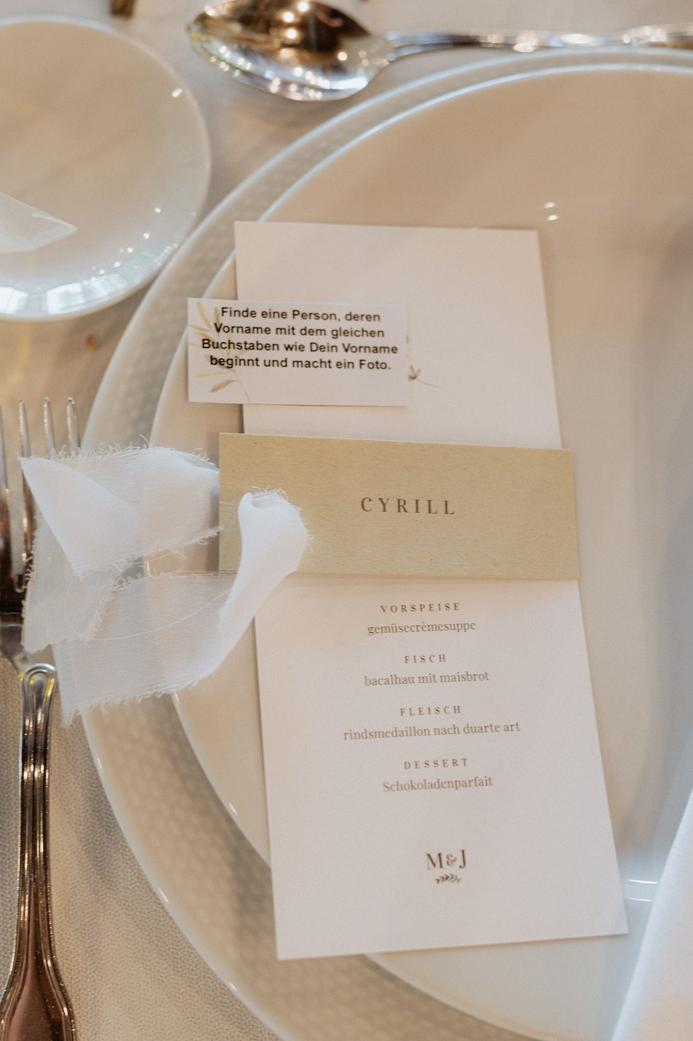 An elegant place setting with a white menu card labeled 'CYRILL' decorated with a silk ribbon on a textured plate.