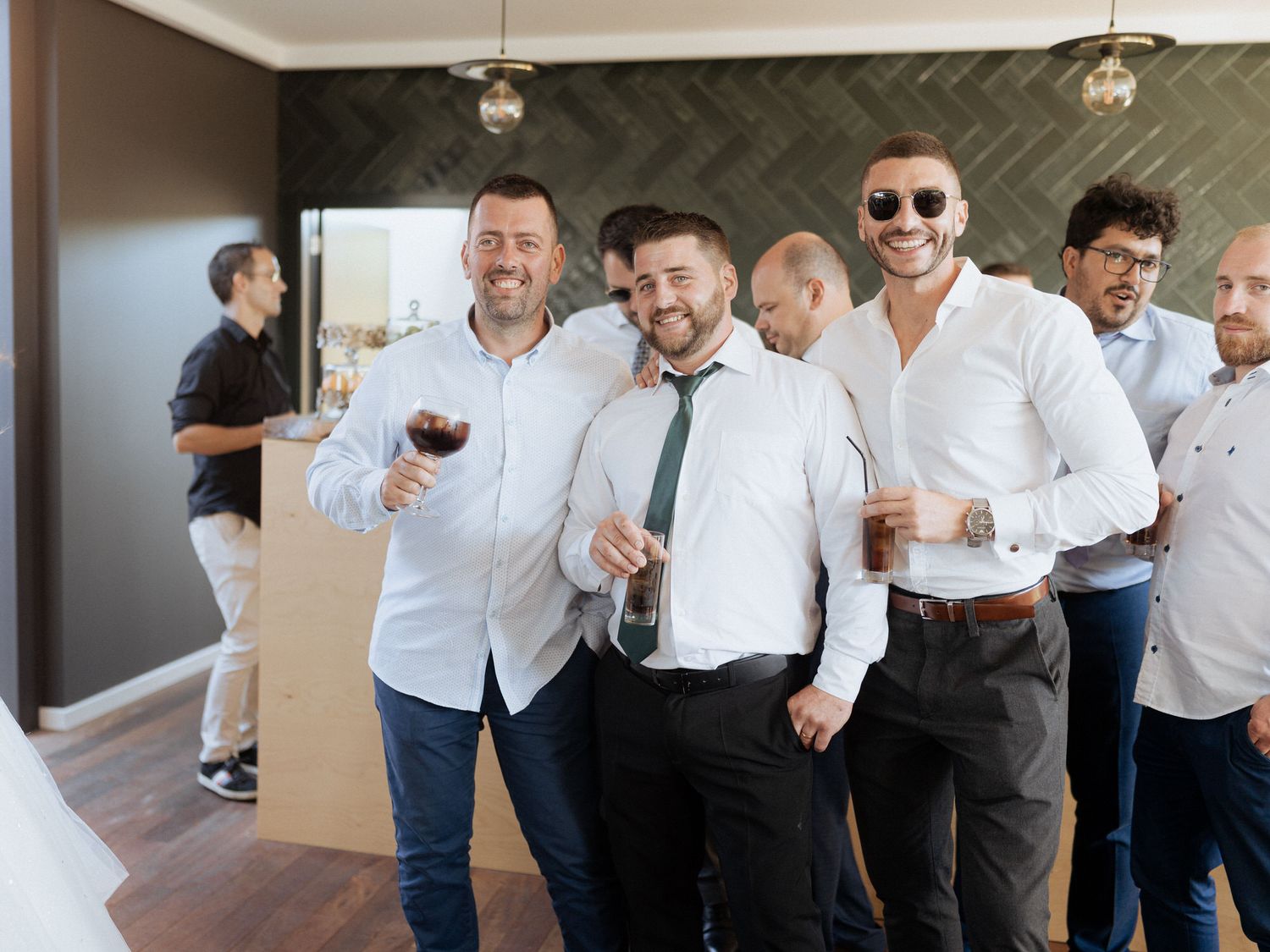 A group of well-dressed men laugh and socialize while holding drinks at an indoor celebration event.