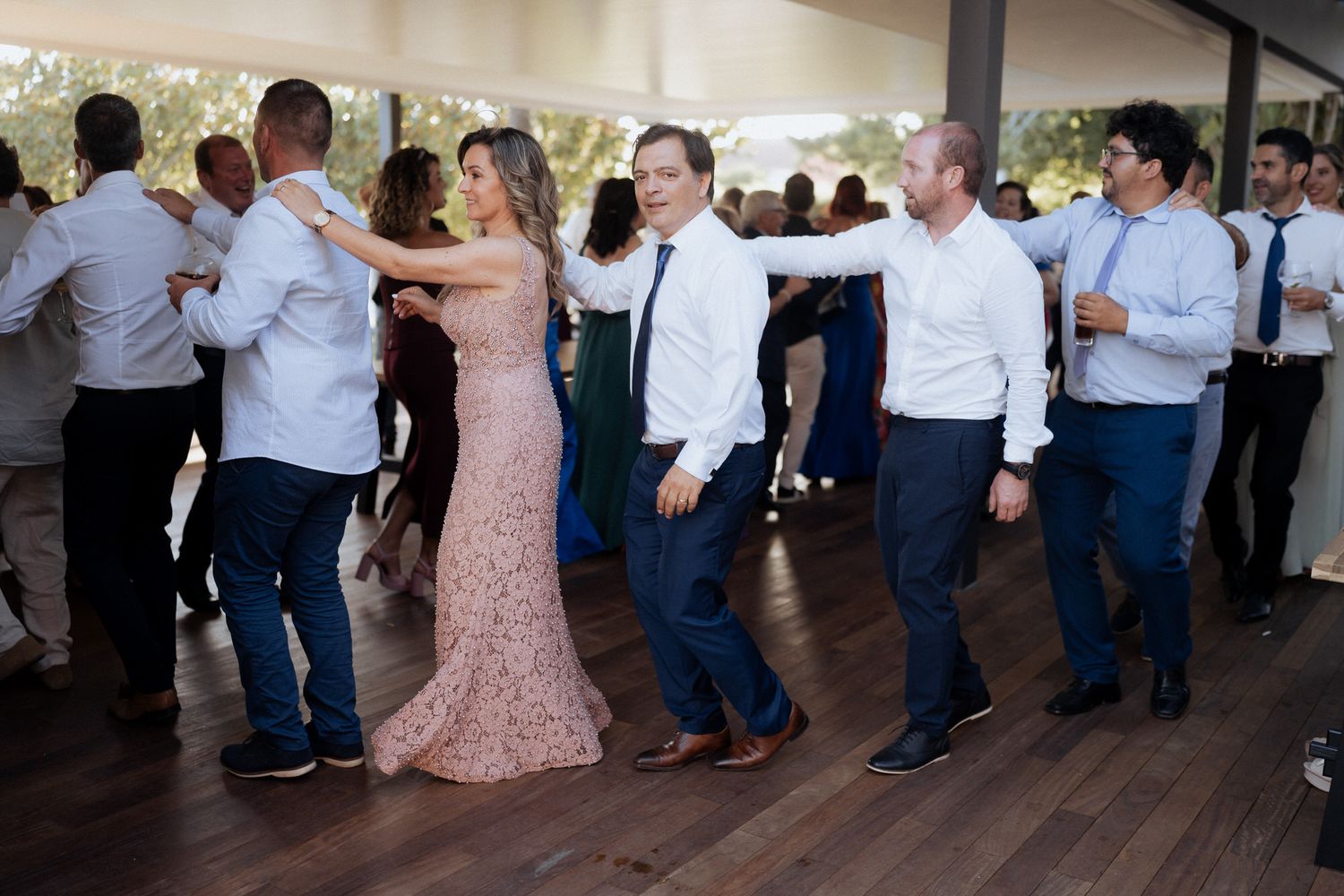 Guests dancing in line during a celebration in a bright indoor venue with blush pink and blue color scheme.