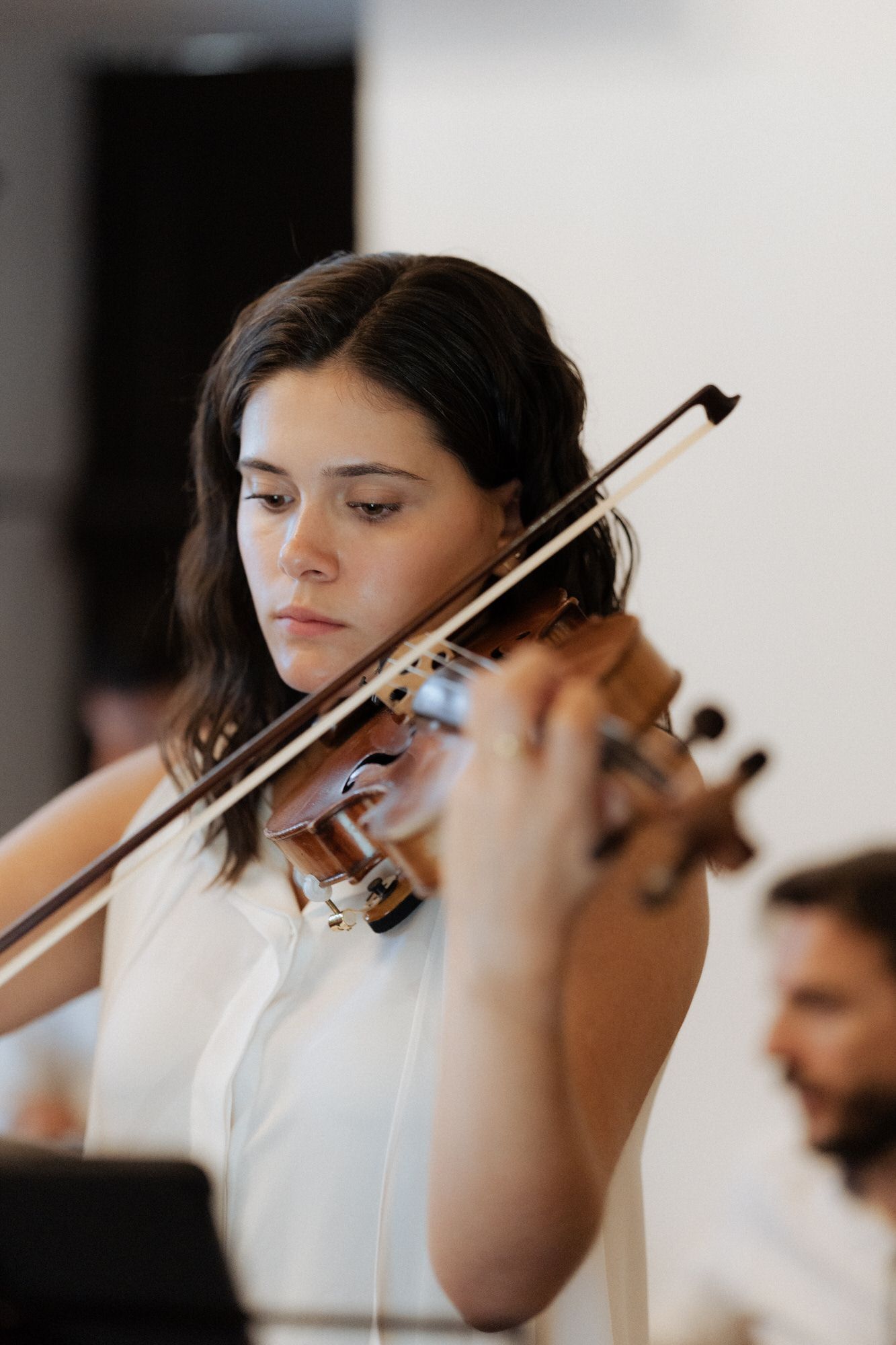 A string musician in a white outfit performs on violin during what appears to be a classical concert or recital.